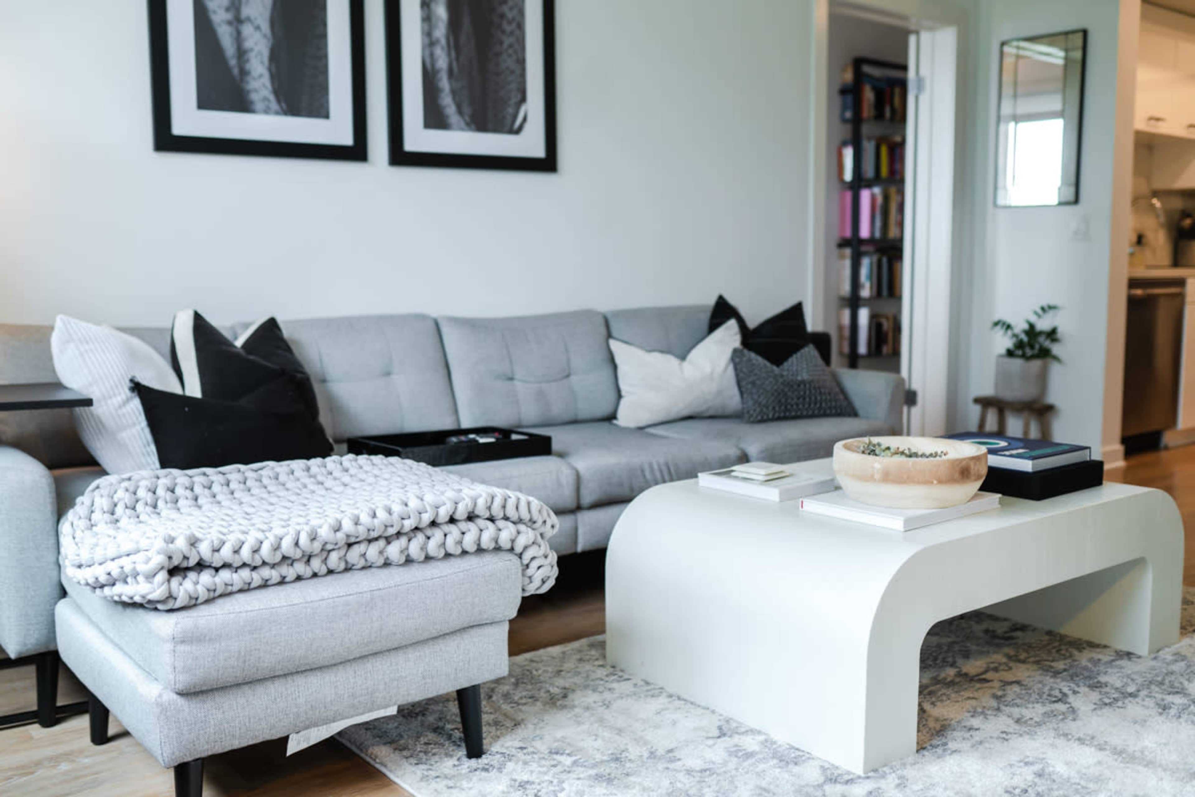 A modern living room featuring a gray sofa with decorative pillows, a white coffee table, and a cozy throw blanket draped over an ottoman.