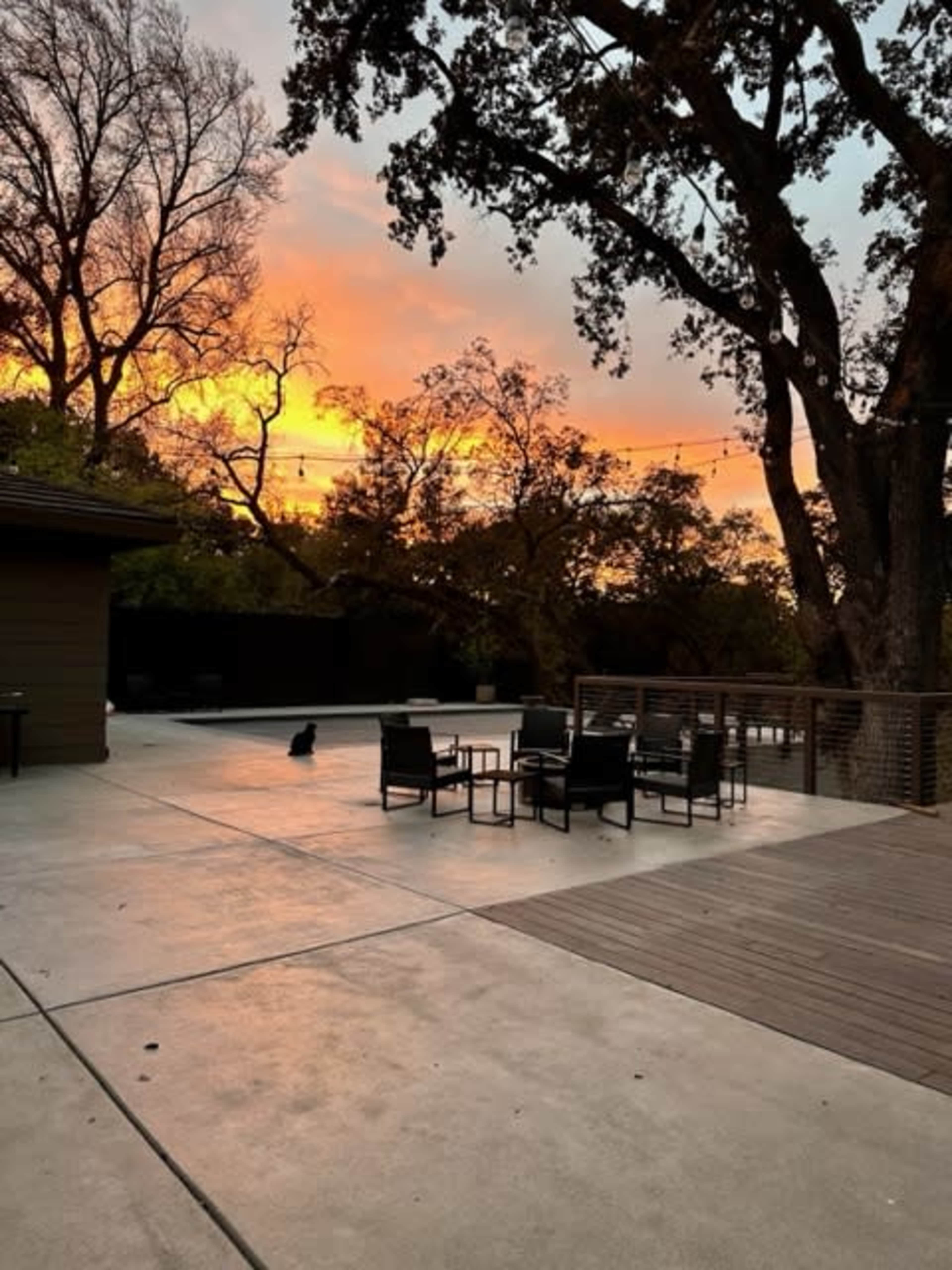A patio with seating arrangements sits under a vibrant sunset, surrounded by trees.