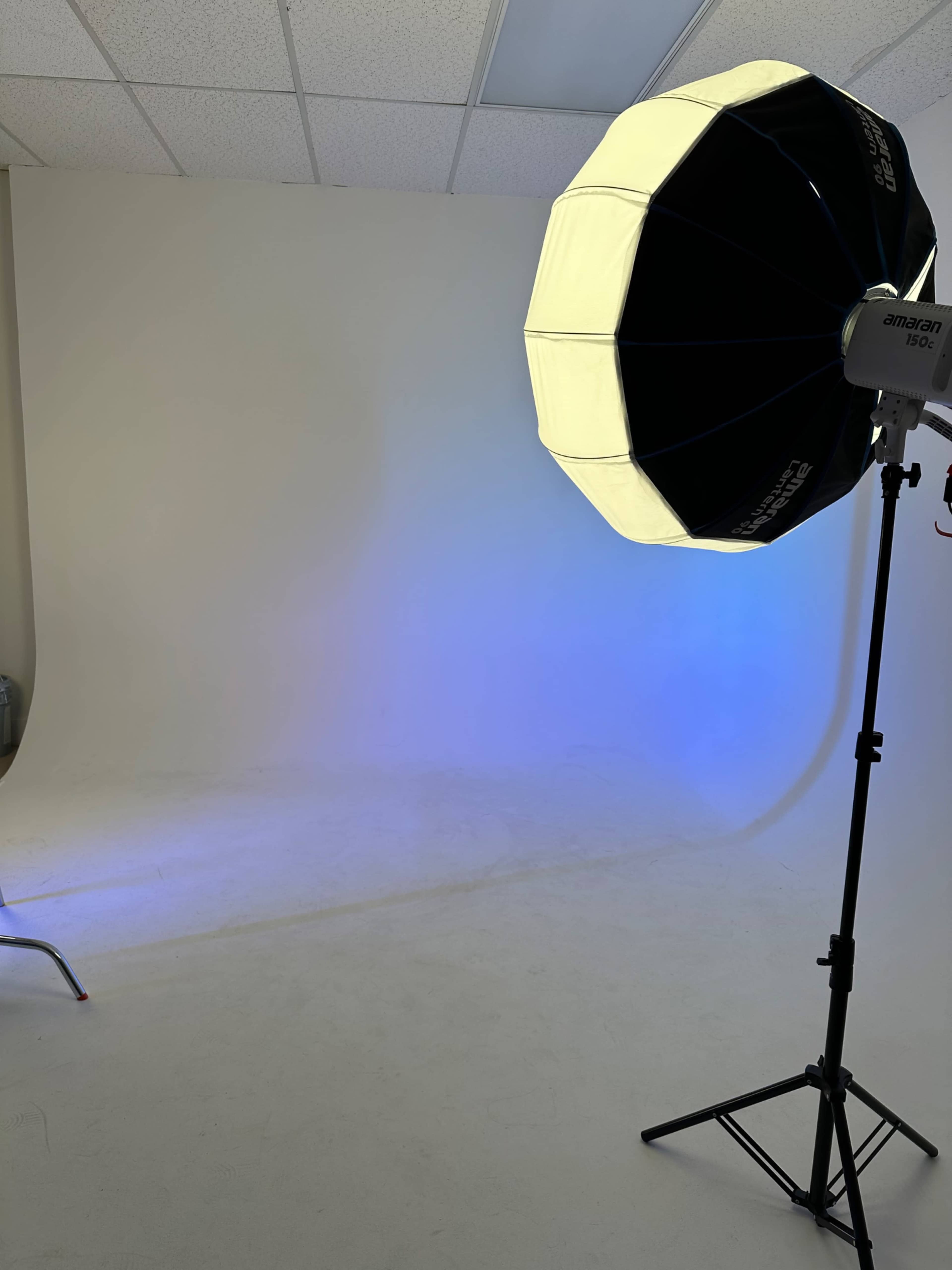 A photography studio features a white backdrop and a large octagonal softbox positioned on a stand.
