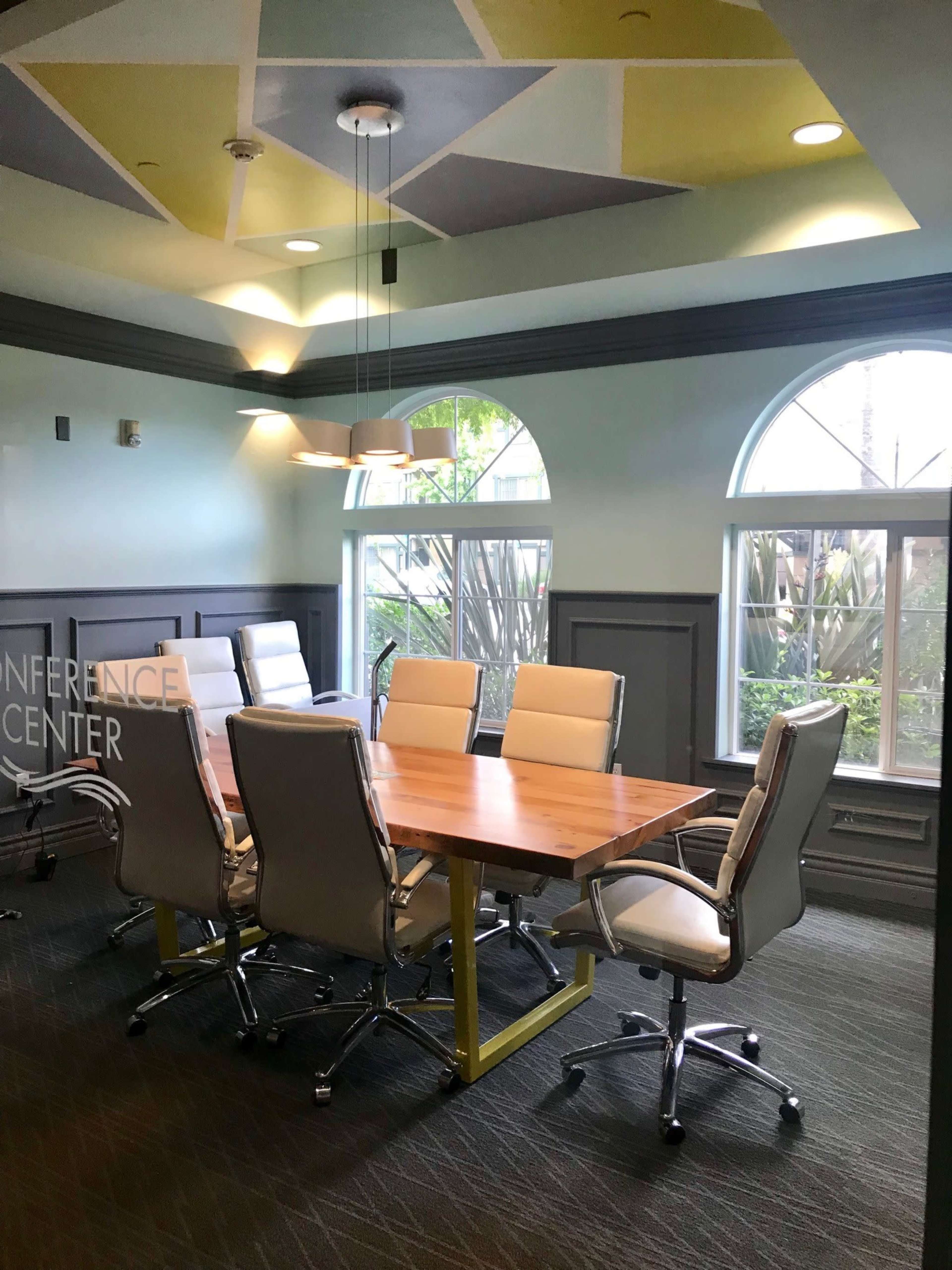 A conference room with a wooden table surrounded by six ergonomic chairs, featuring large windows that allow natural light to fill the space.