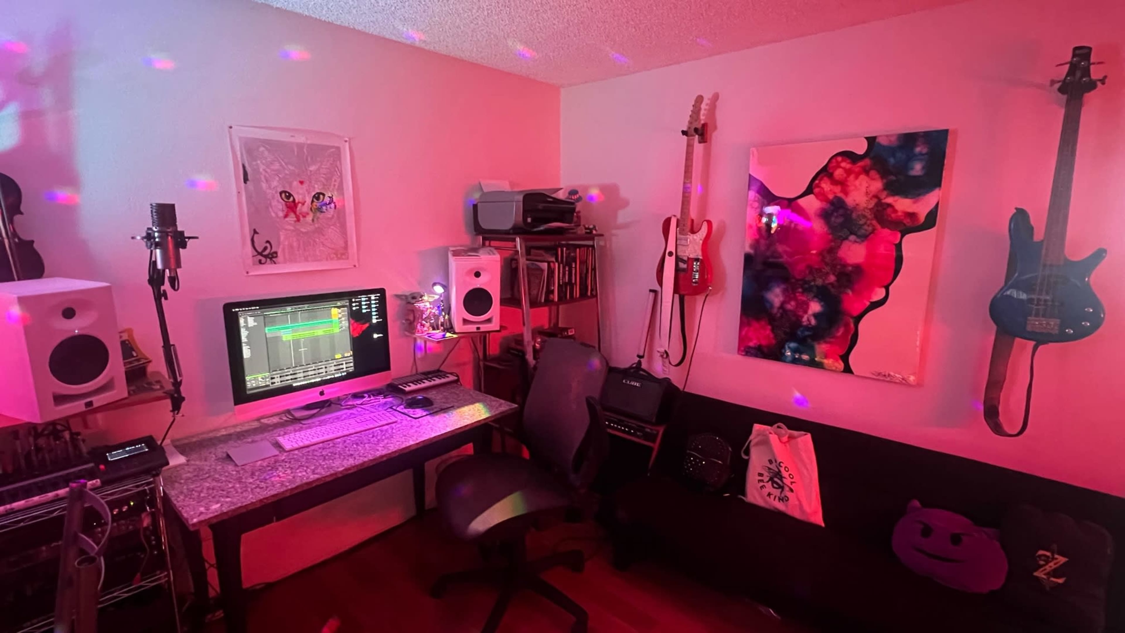 A music studio features a computer setup with audio equipment, guitars mounted on the wall, and colorful lighting effects.