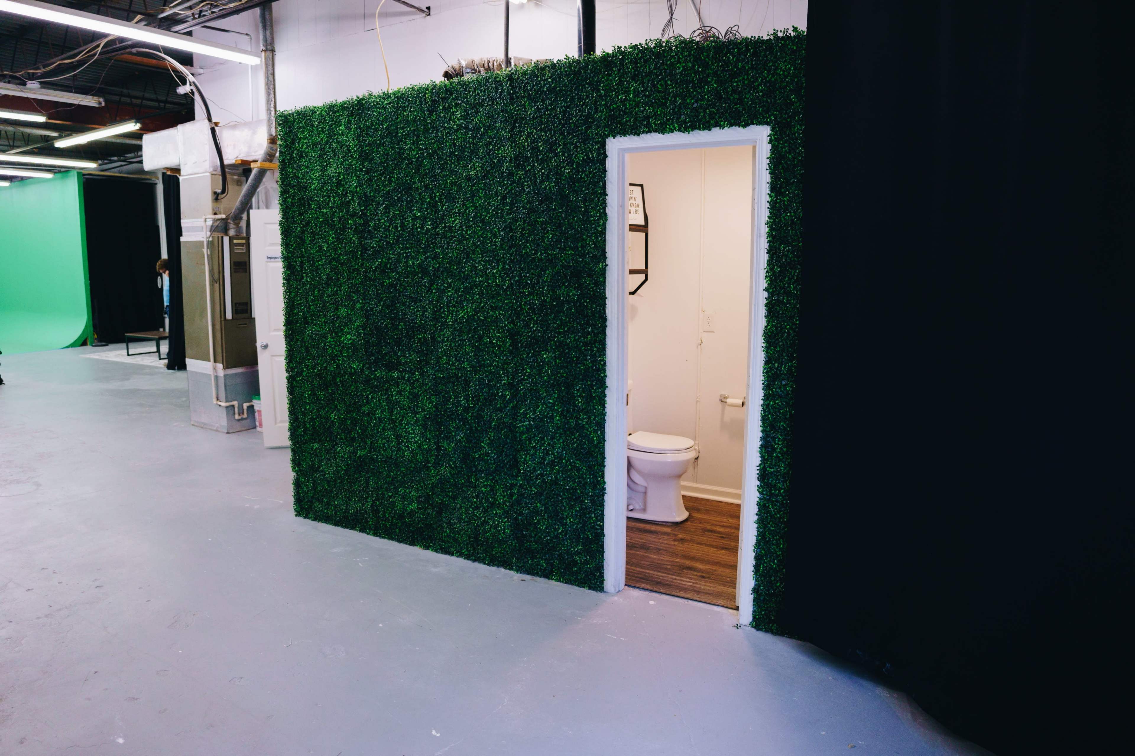 A green artificial grass wall with an open doorway leading to a bathroom area.