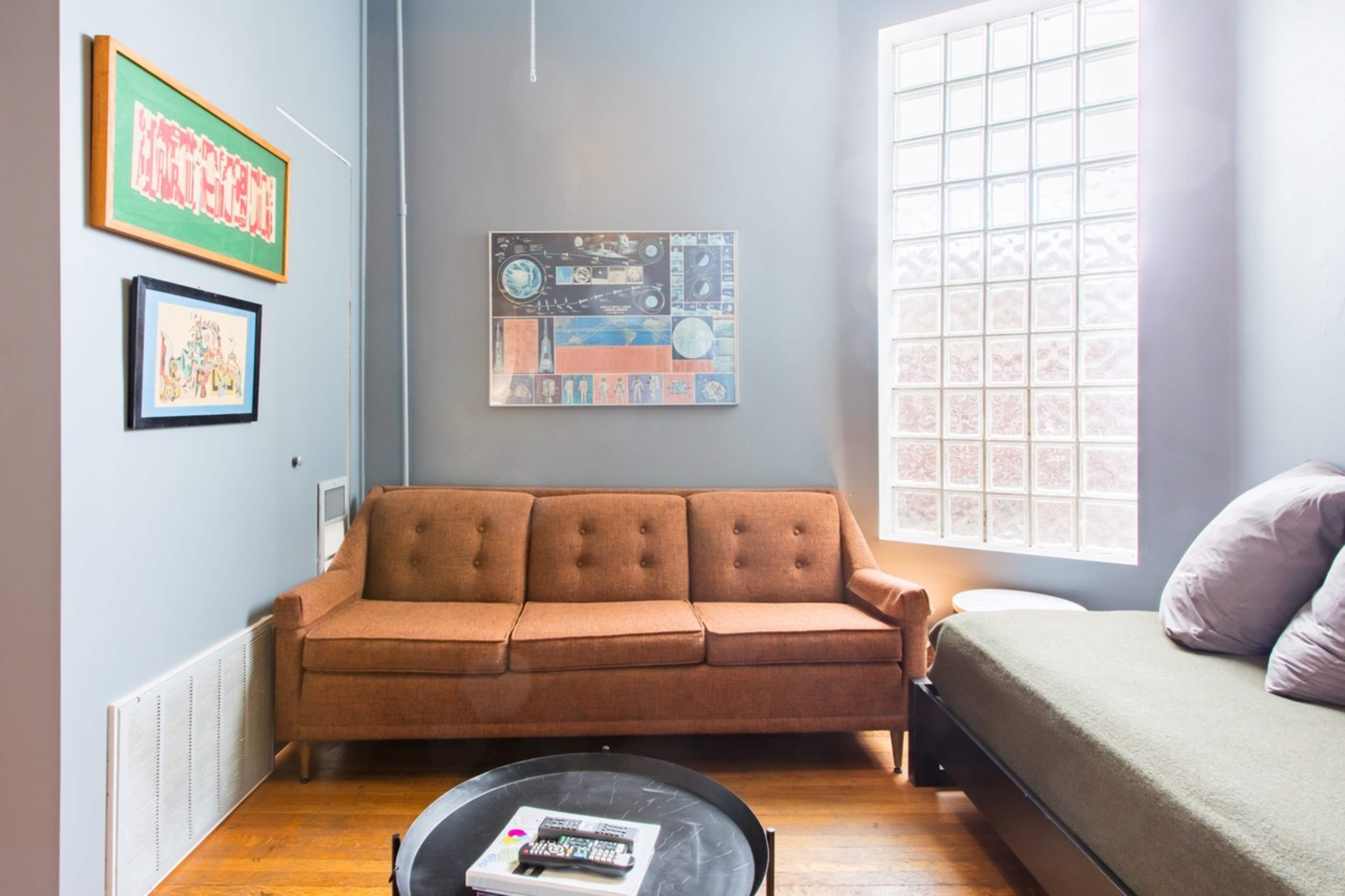 A cozy living room featuring a brown sofa, a glass block window, and a round coffee table with magazines.