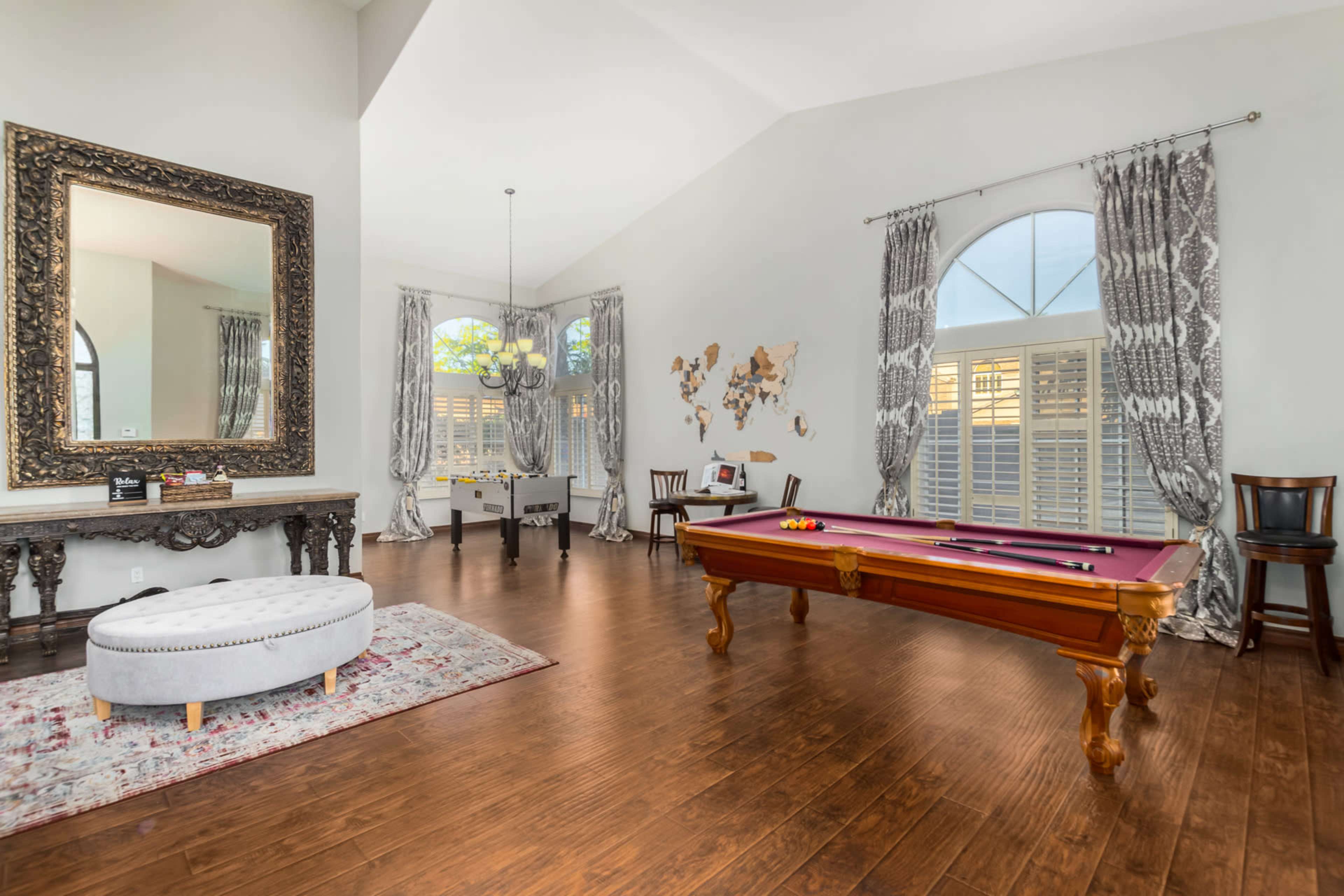 The room features a pool table, a large decorative mirror, and a world map on the wall, with elegant curtains framing the windows.