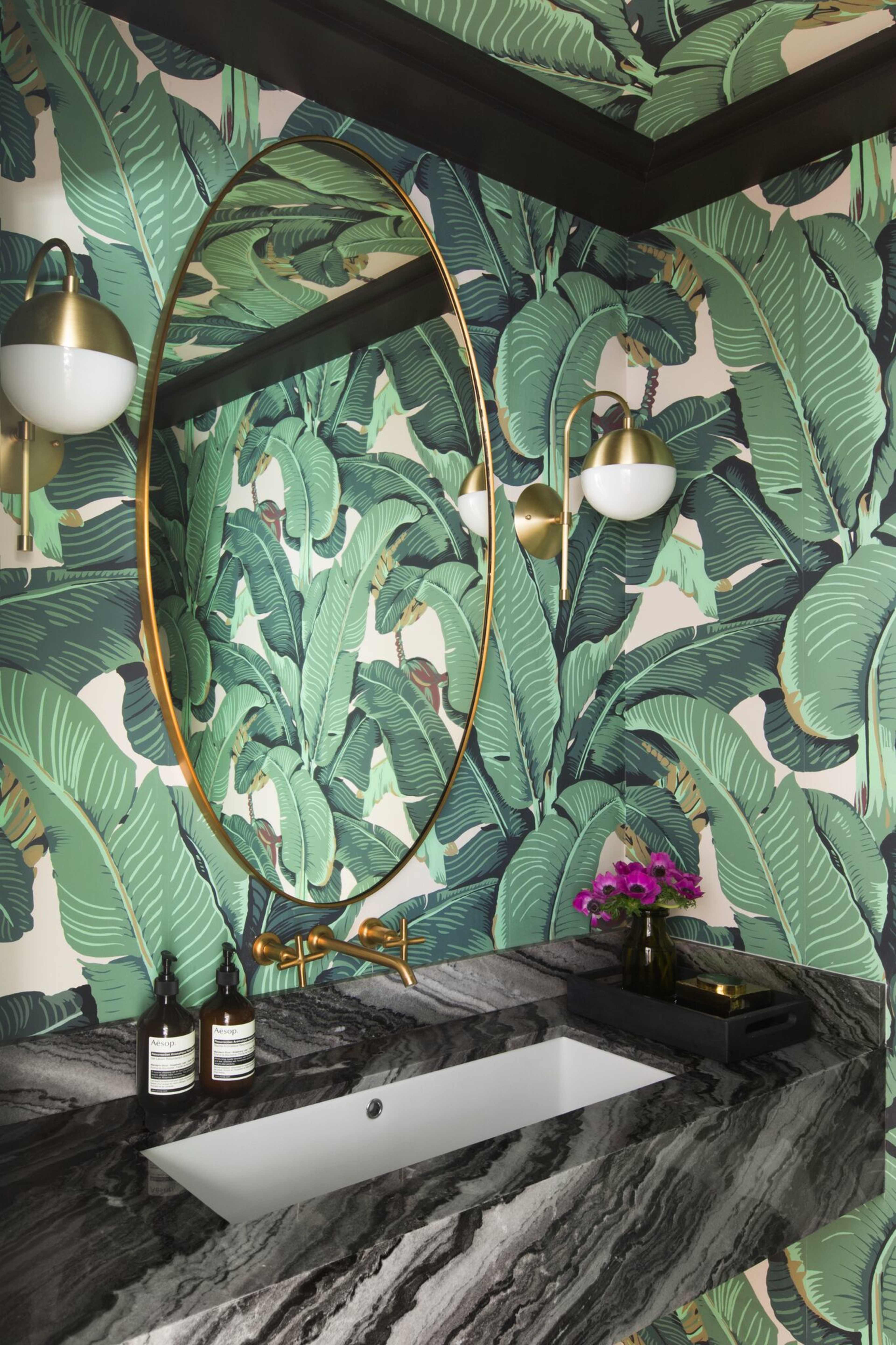 The bathroom features a black and white striped marble countertop with a rectangular sink, surrounded by green tropical leaf wallpaper and an oval gold-framed mirror.