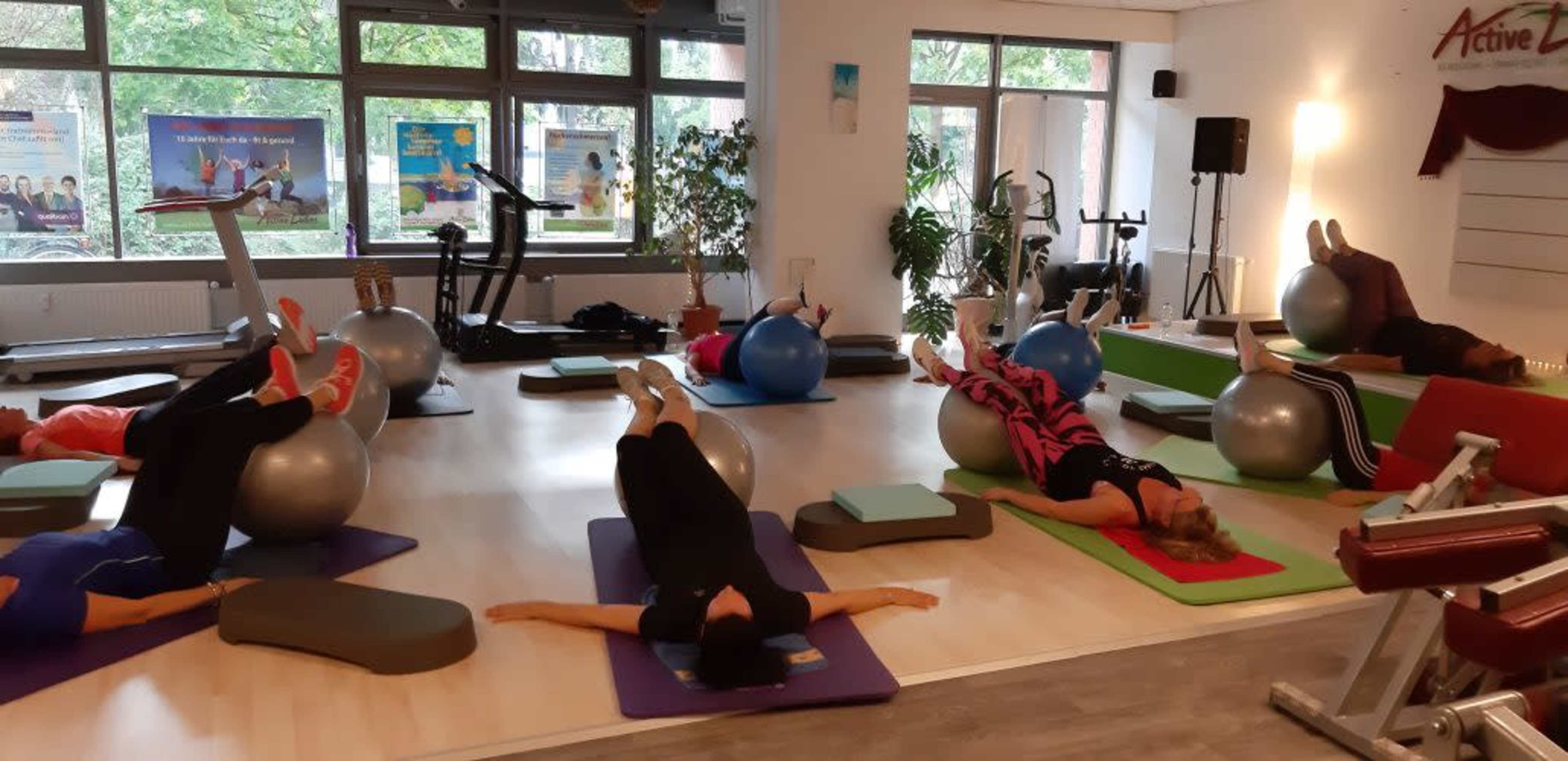 A group of people exercises on stability balls and mats in a gym setting.