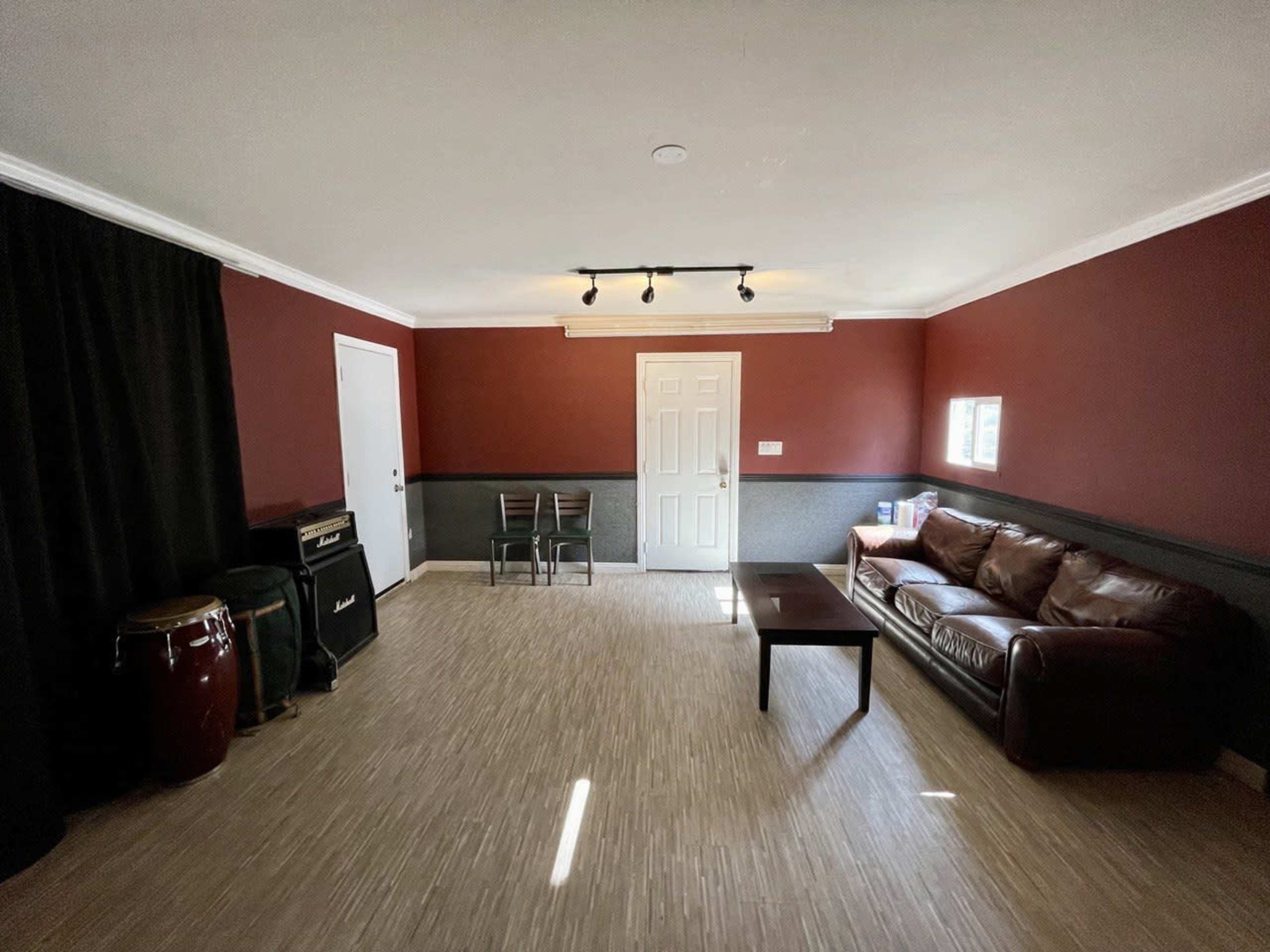 The room features dark red walls, a brown leather couch, a coffee table, and musical instruments in one corner.
