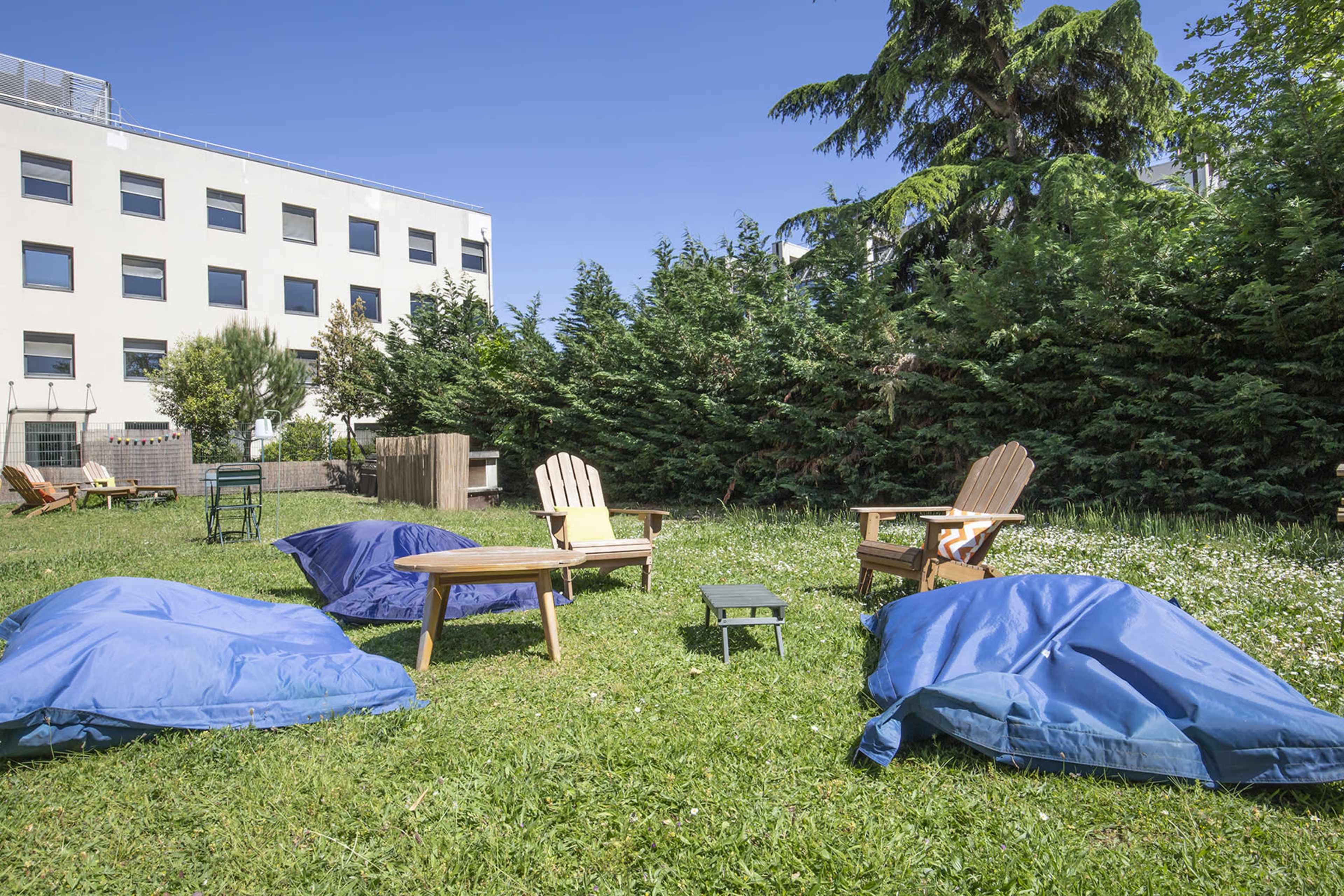 A grassy area with two wooden chairs, a small table, and several blue bean bag chairs under a clear blue sky.