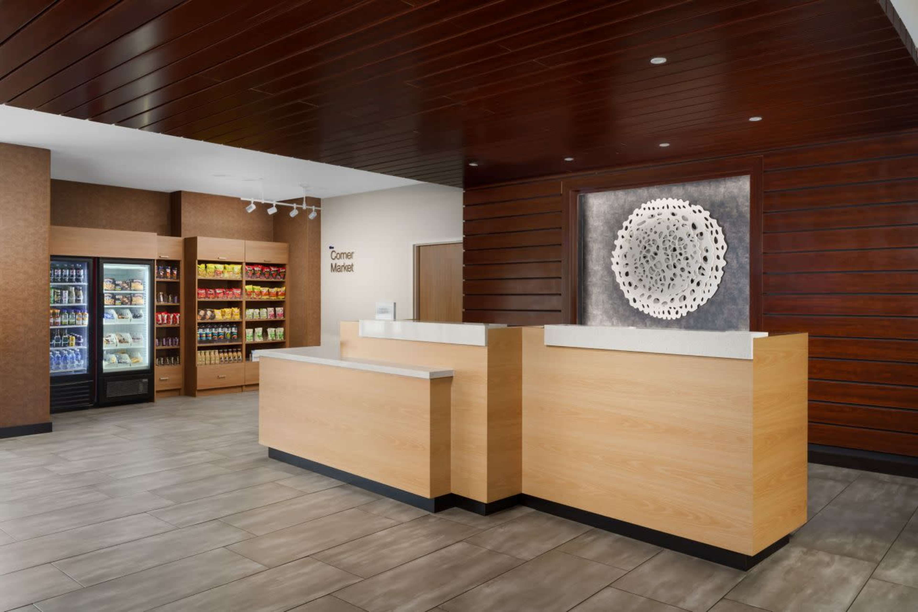 The image features a modern reception area with a wooden front desk, a wall display, and a background vending machine section.