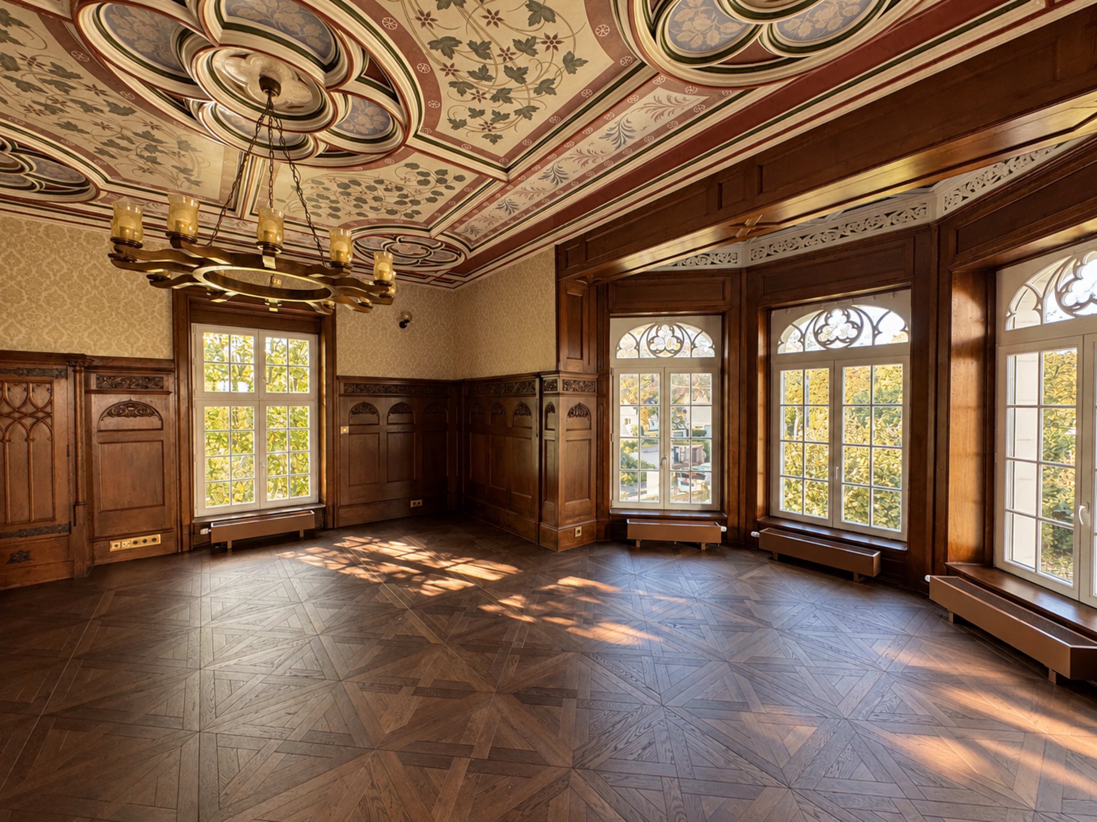 The image shows a spacious room with wooden paneling, large windows, and a decorative ceiling featuring floral patterns.