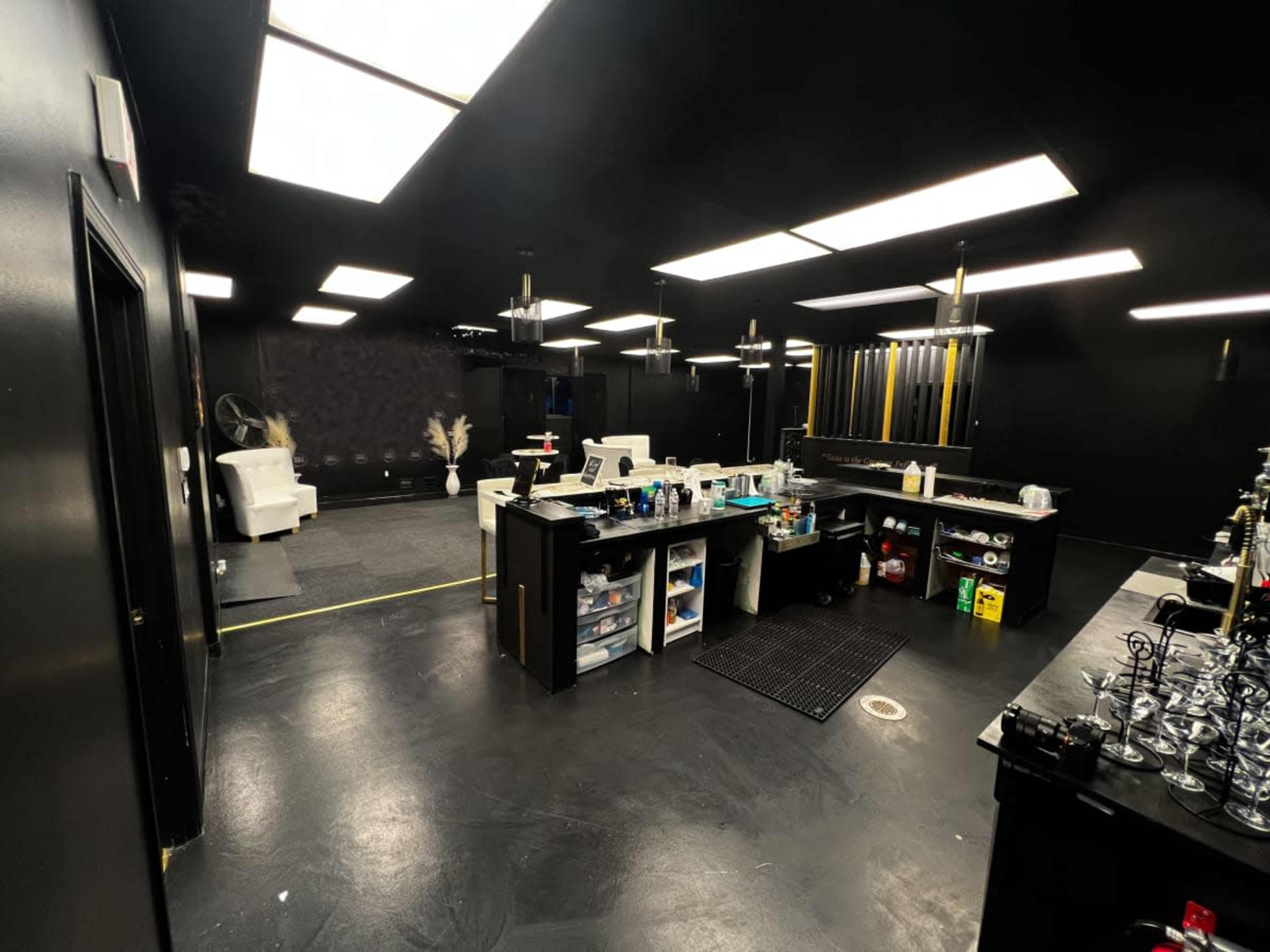 A darkly-themed interior of a modern lounge or preparation area featuring a black floor, black walls, and a well-organized counter with various tools and supplies.