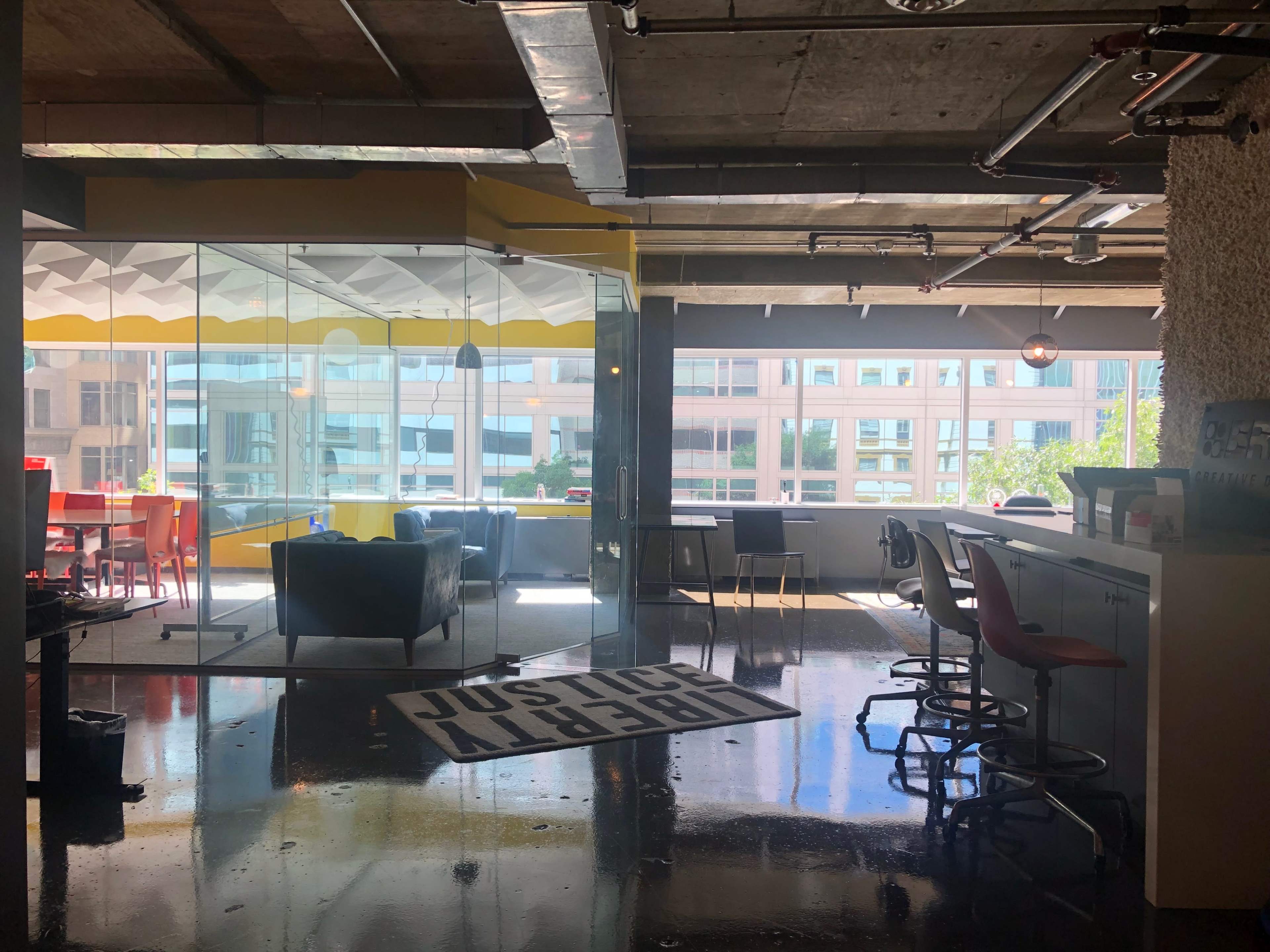 A modern office space with open areas, glass walls, and a mix of seating options.