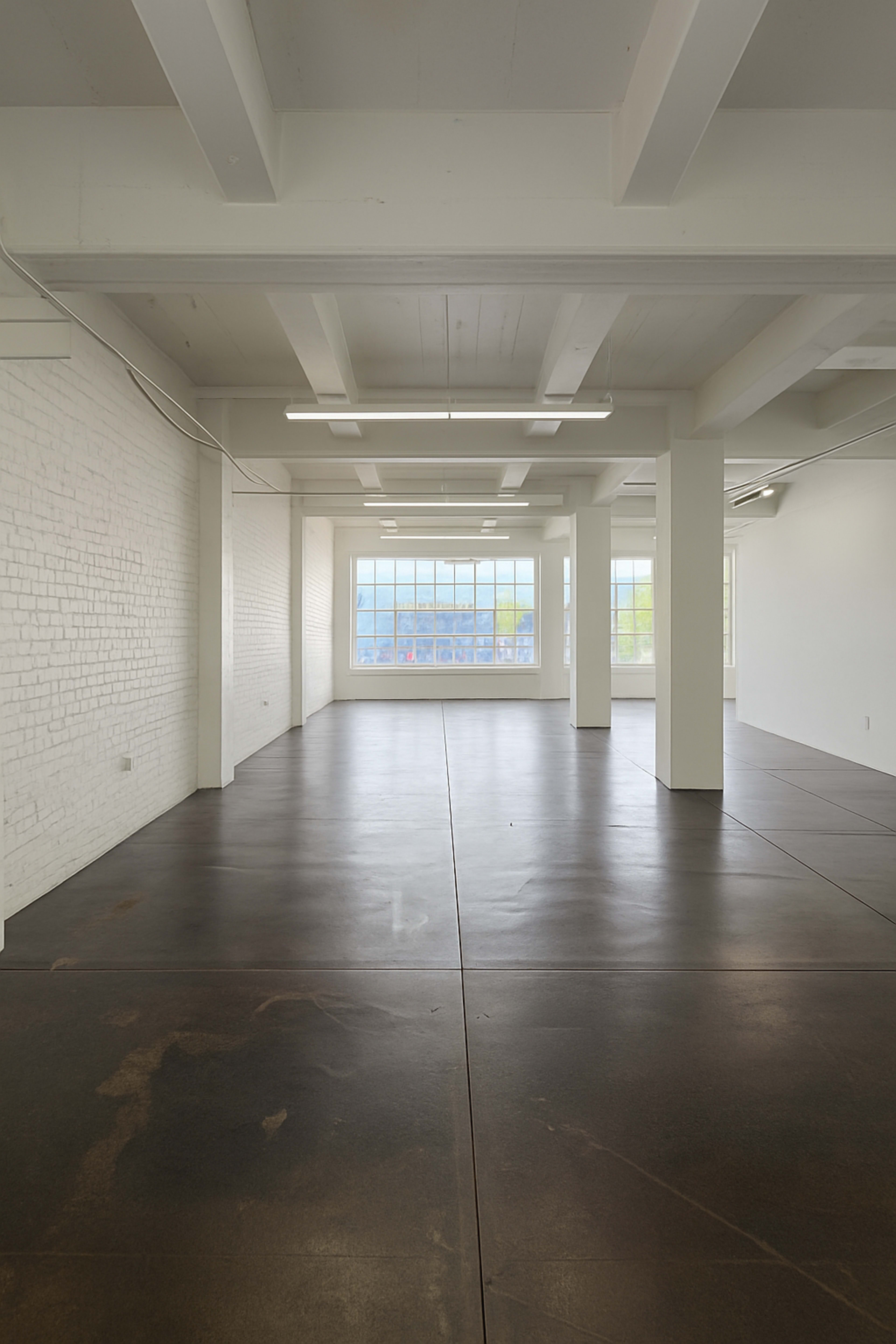 The image shows an empty industrial space with white brick walls, large windows, and a polished concrete floor.