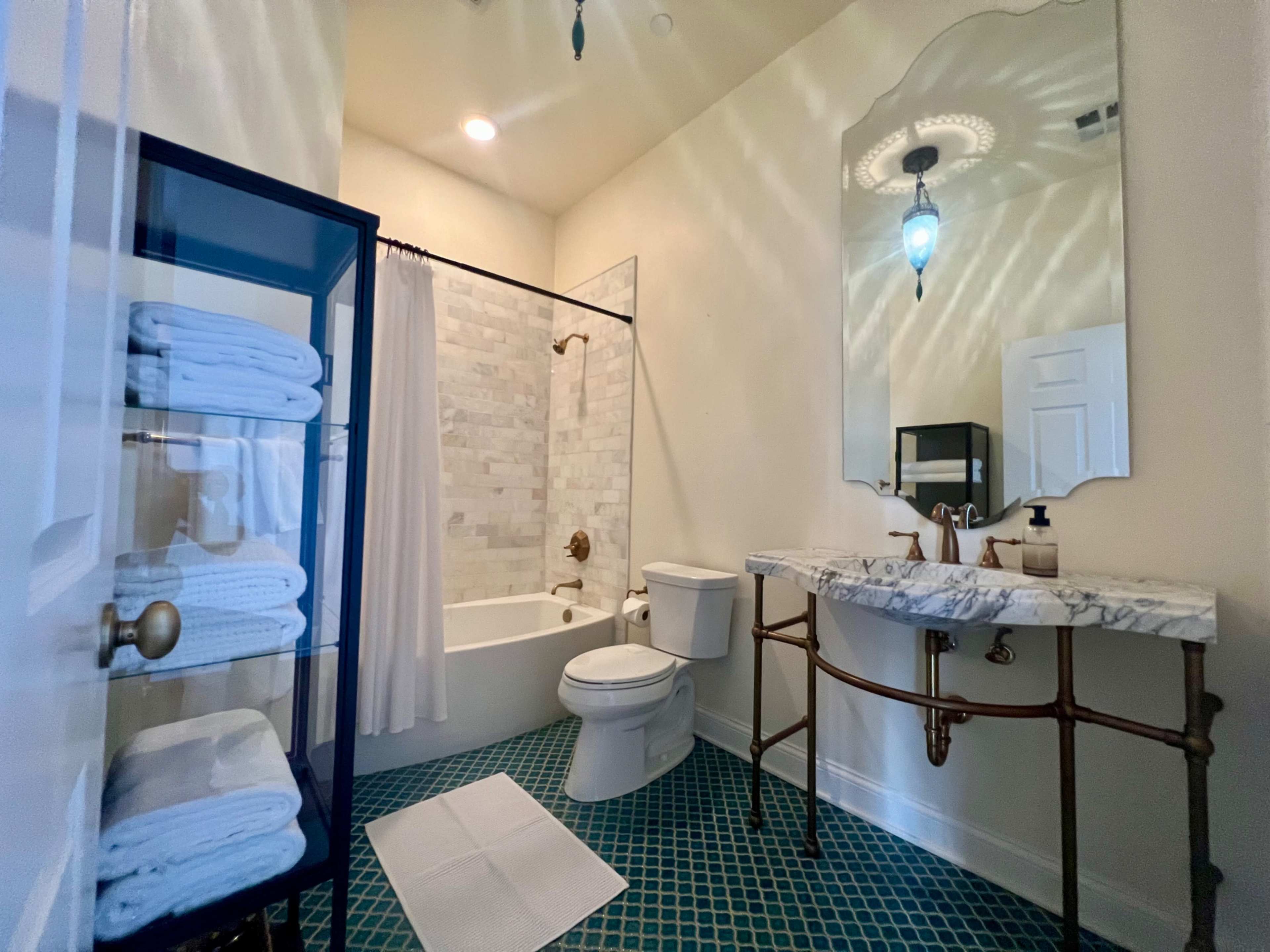 A bathroom featuring a shower-tub combo, a toilet, a marble sink on a metal frame, and neatly stacked white towels.