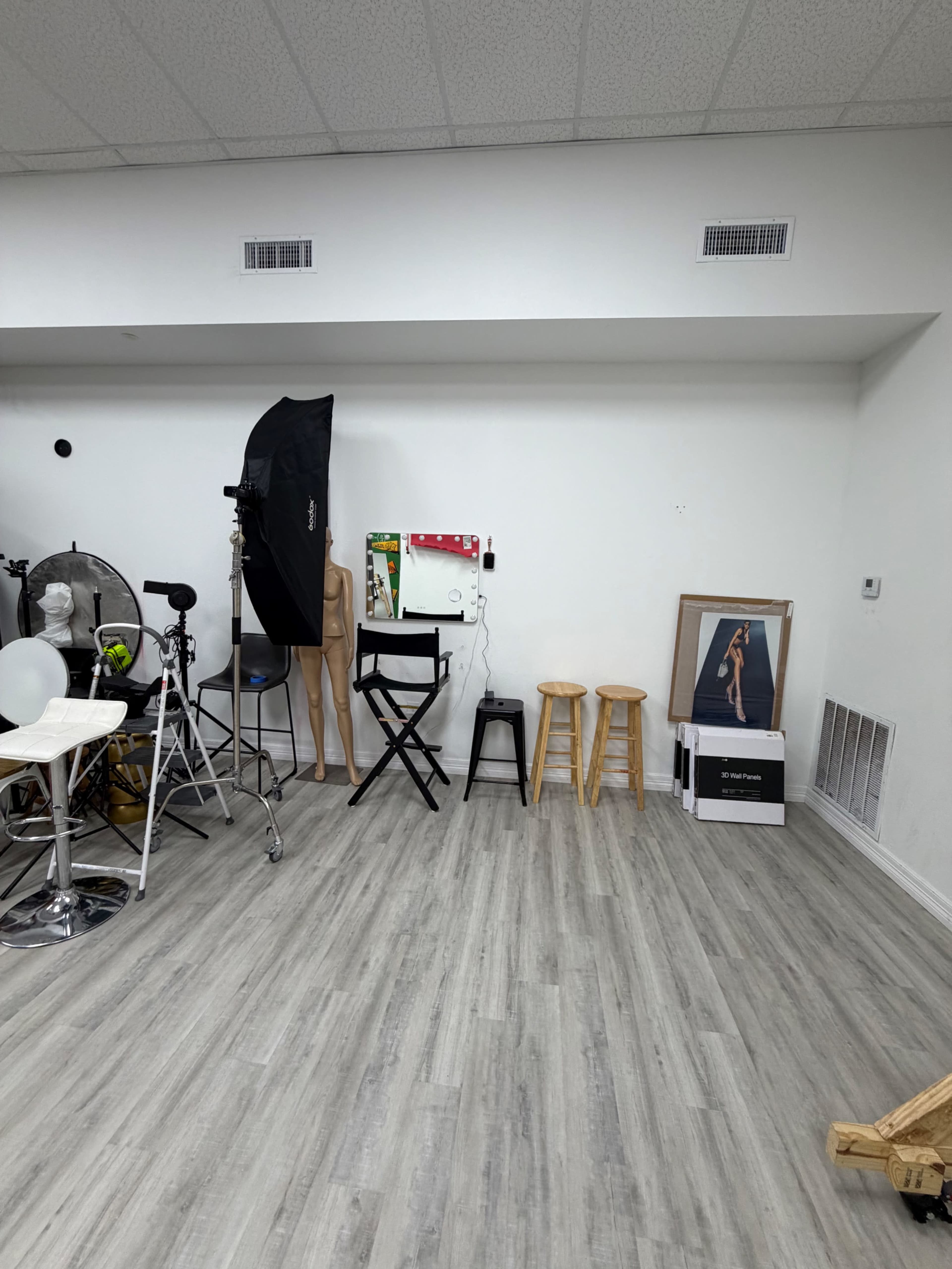 The image shows a photography studio featuring various equipment, including lights, a posing mannequin, stools, and a large wall mirror.