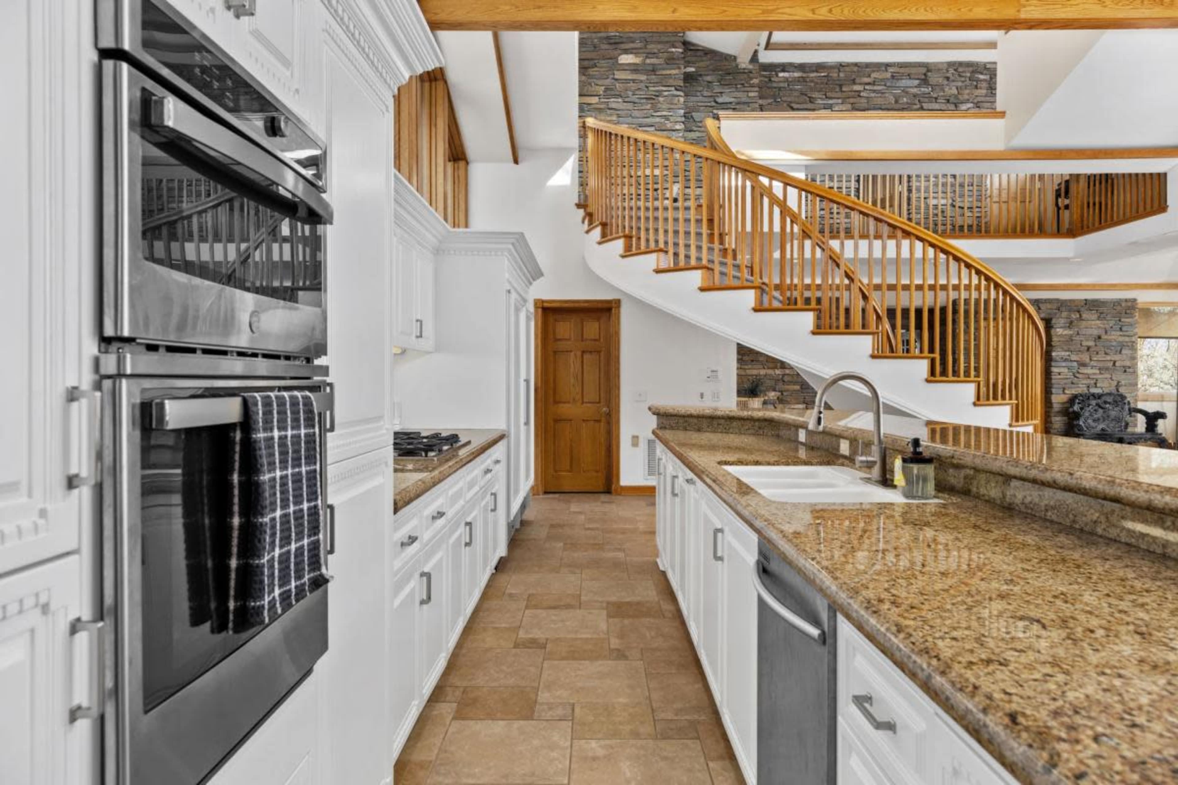 A modern kitchen with granite countertops, stainless steel appliances, and a wooden staircase leading to an upper level.