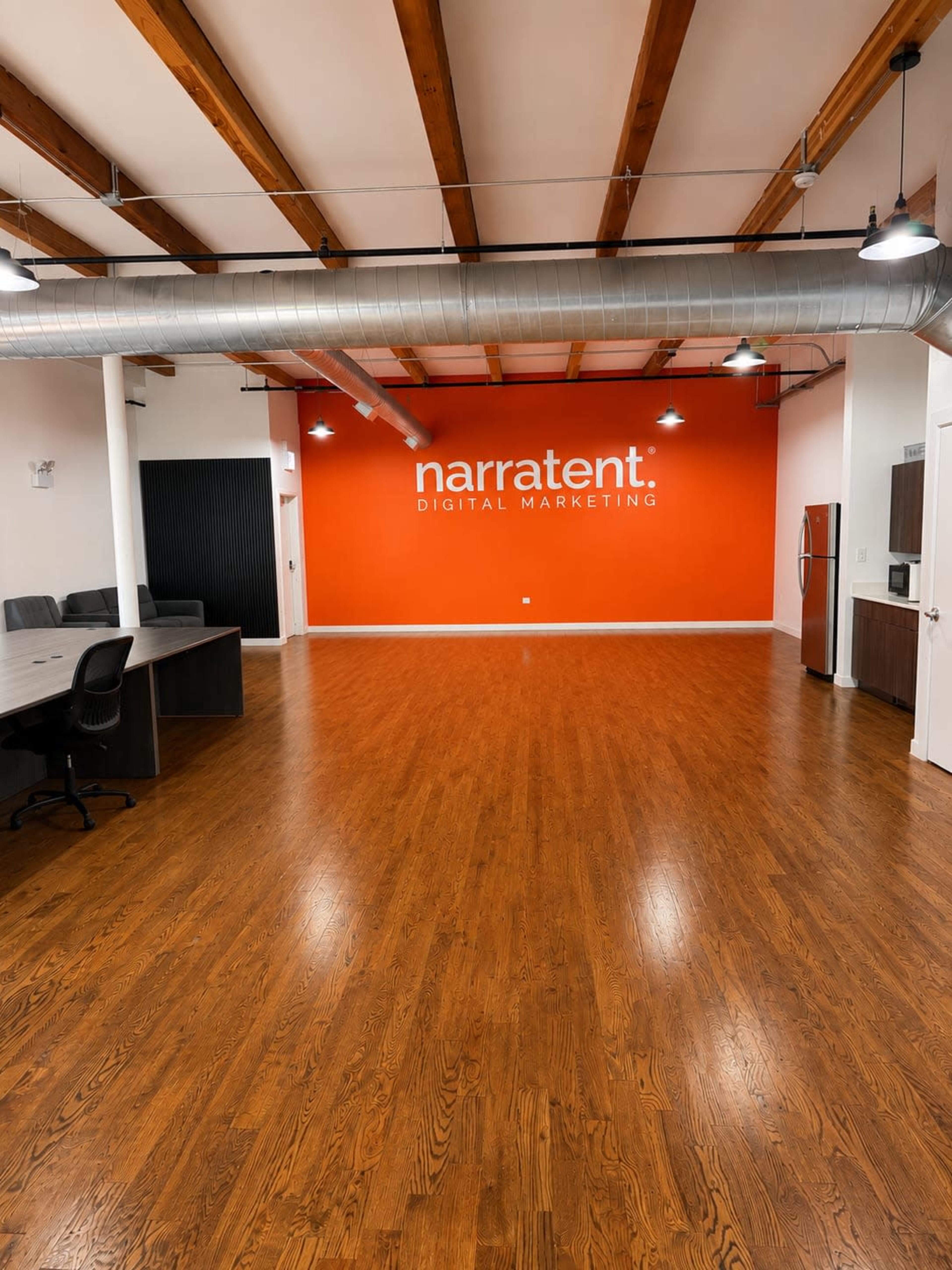 The image shows a spacious office interior with wooden flooring and an orange wall featuring the text "narratent DIGITAL MARKETING."