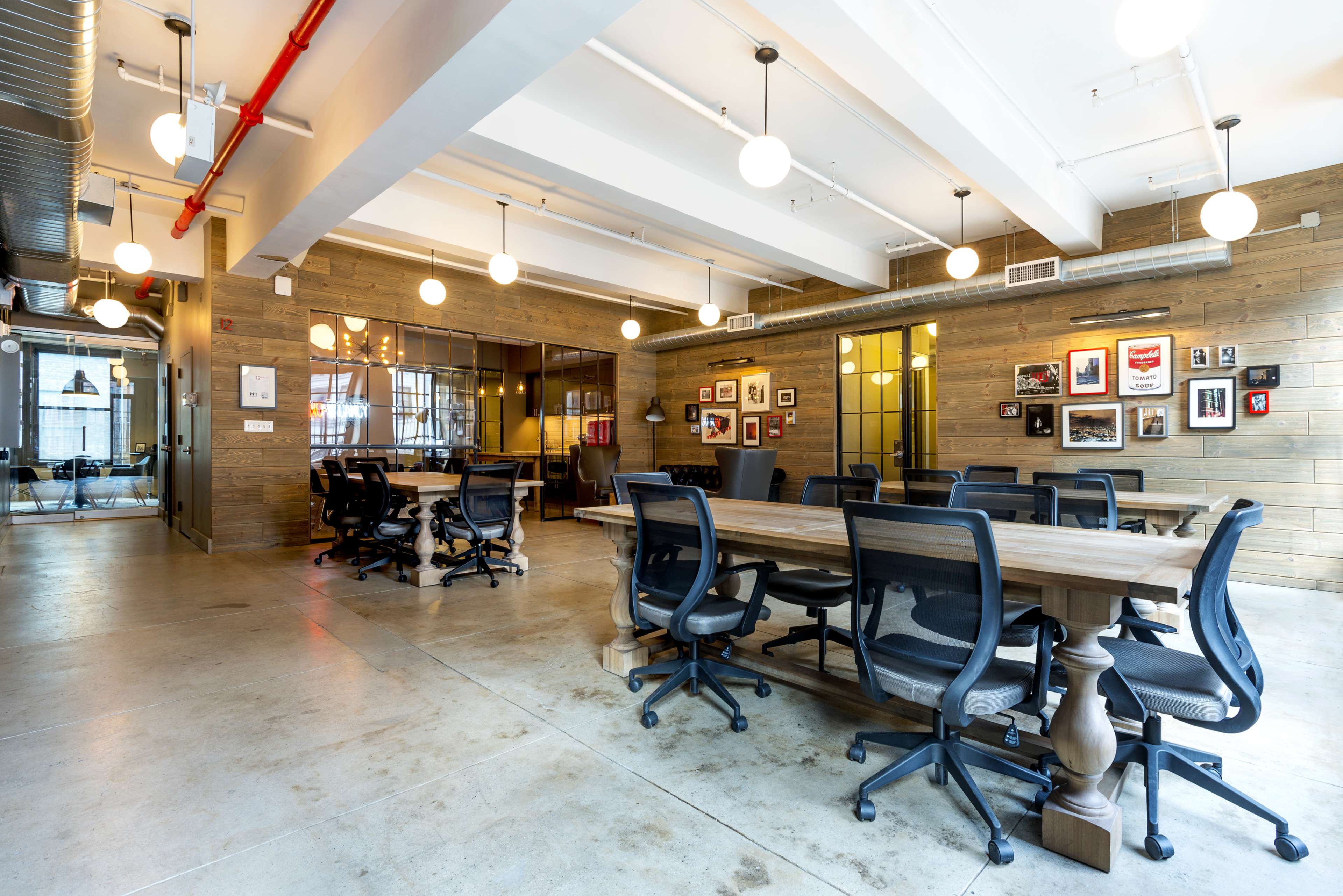 The image shows a modern conference room with a long wooden table surrounded by black office chairs, featuring exposed light fixtures and wooden walls adorned with framed pictures.