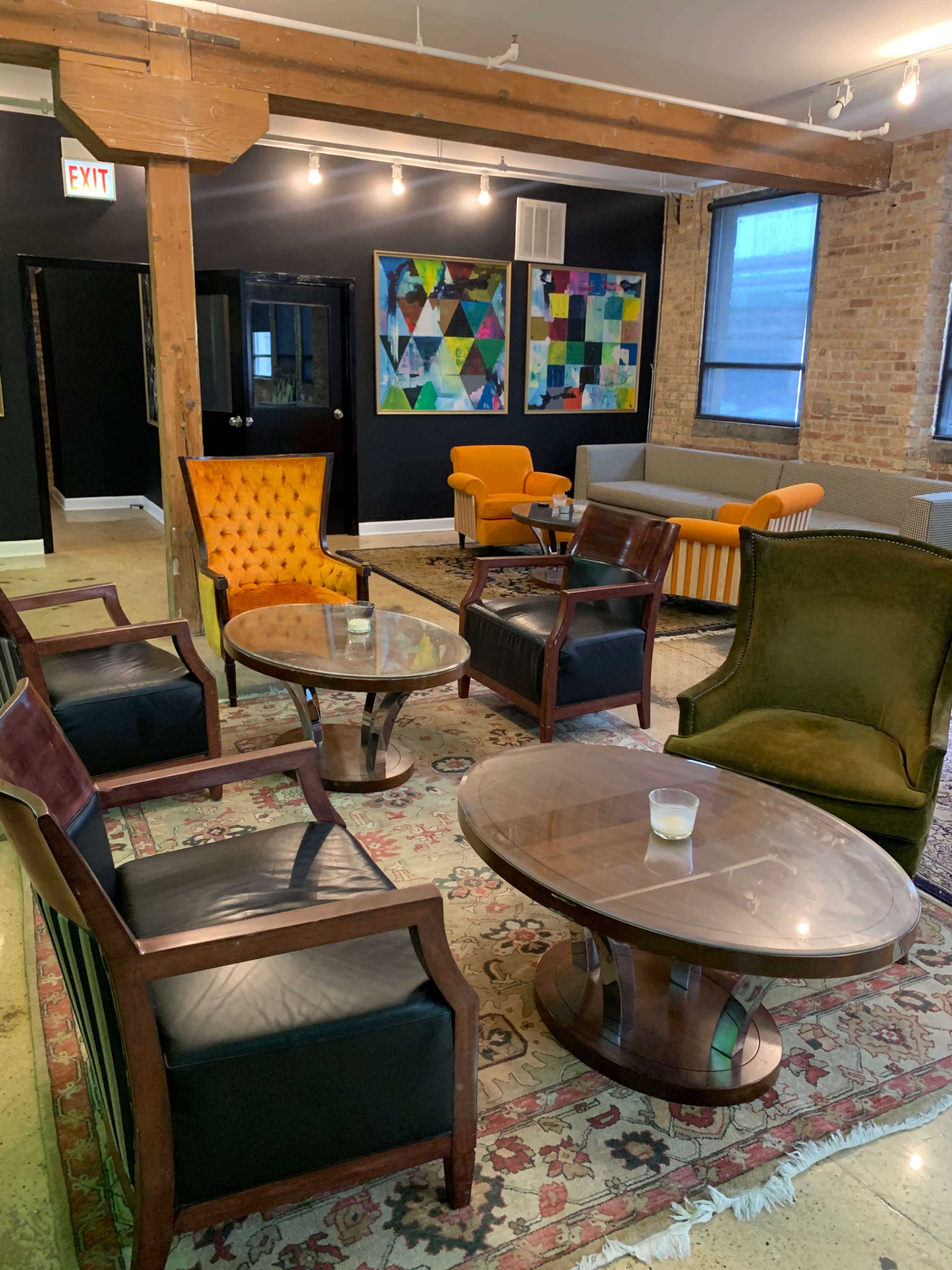 A cozy lounge area features various seating options, including colorful armchairs and a patterned rug, with distinct artwork on the walls.