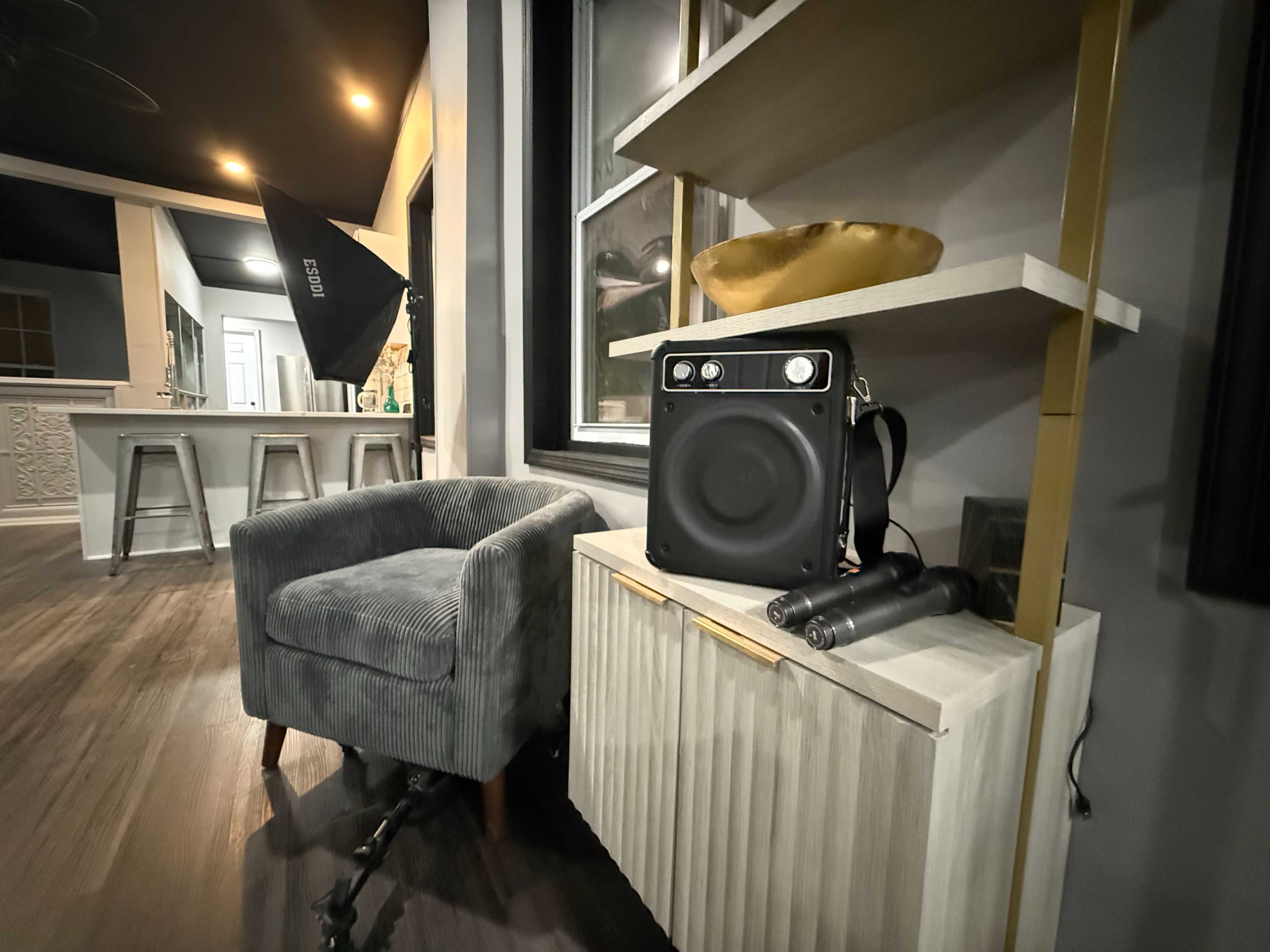 A small gray armchair sits next to a white cabinet displaying a speaker and microphone in a well-lit room.