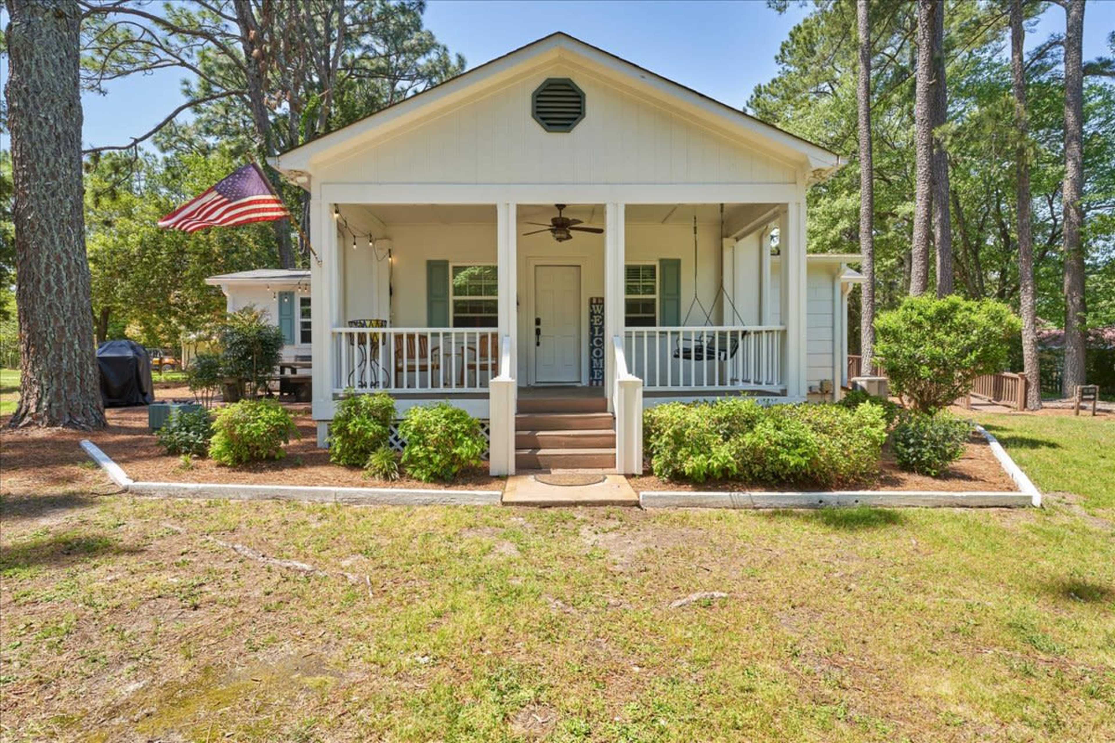 A white house with a covered porch and an American flag stands among trees in a grassy yard.