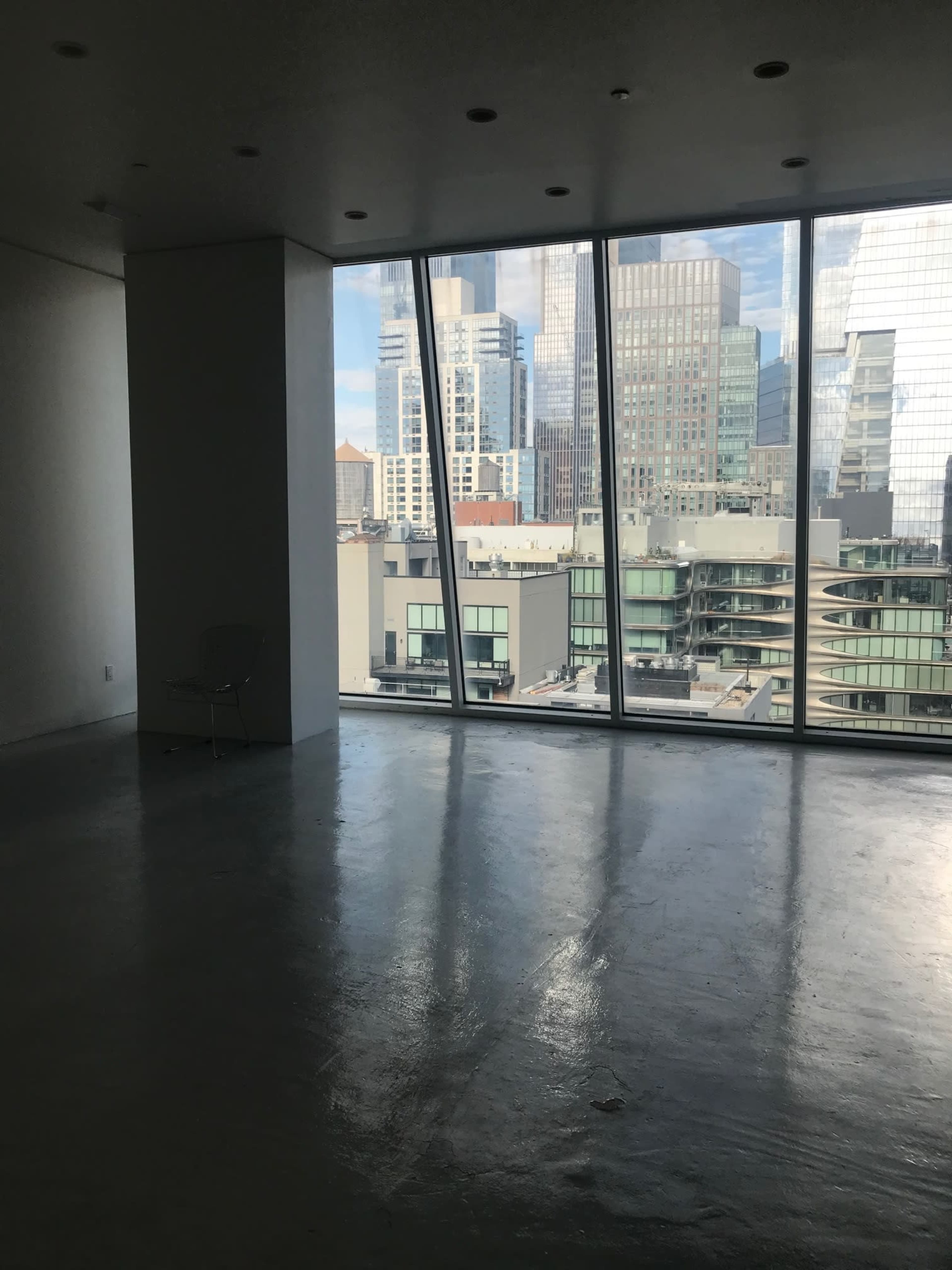 An empty room with a polished concrete floor and large windows overlooking a city skyline.
