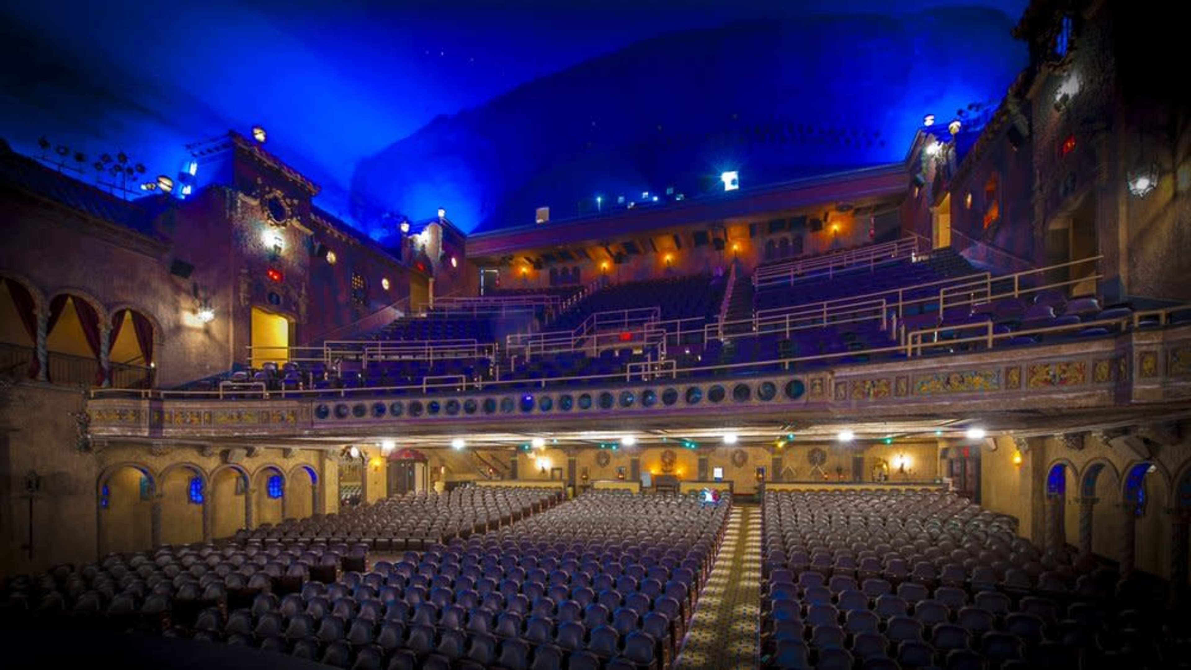 The image showcases an empty theater with rows of seats, ornate architectural details, and a blue-lit ceiling.