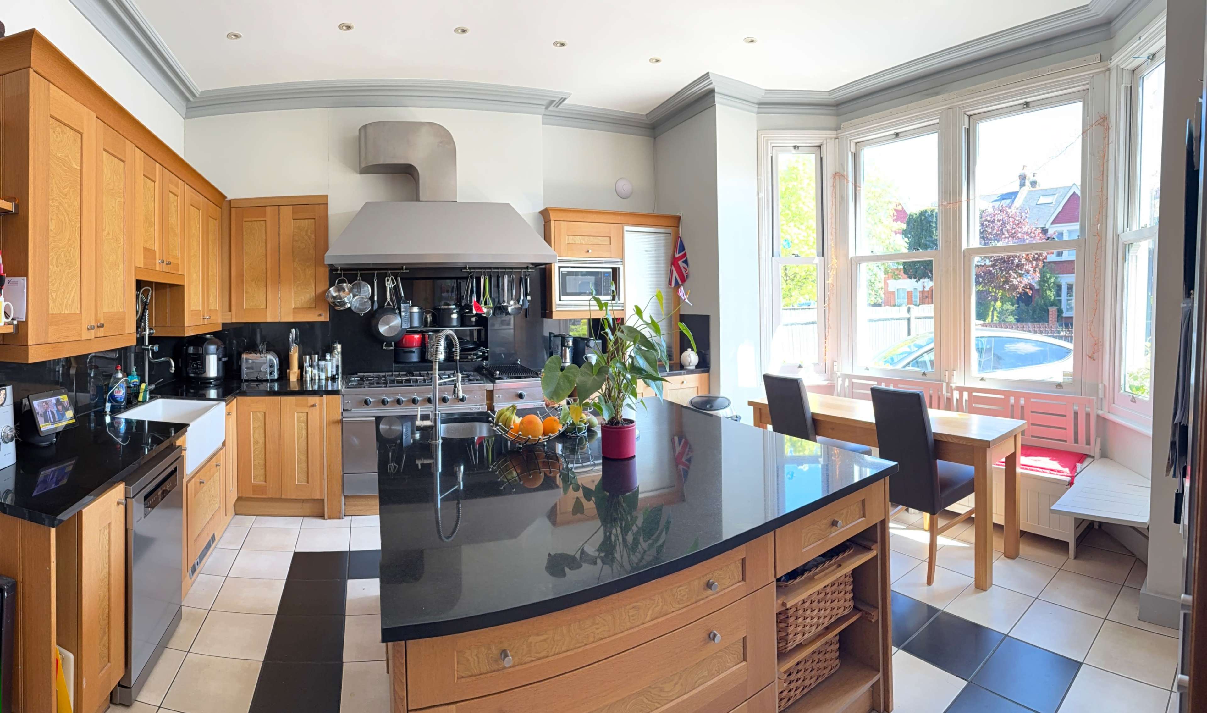 The image shows a spacious kitchen with wooden cabinetry, a large island, and a contrasting black countertop, featuring a dining area by the window.