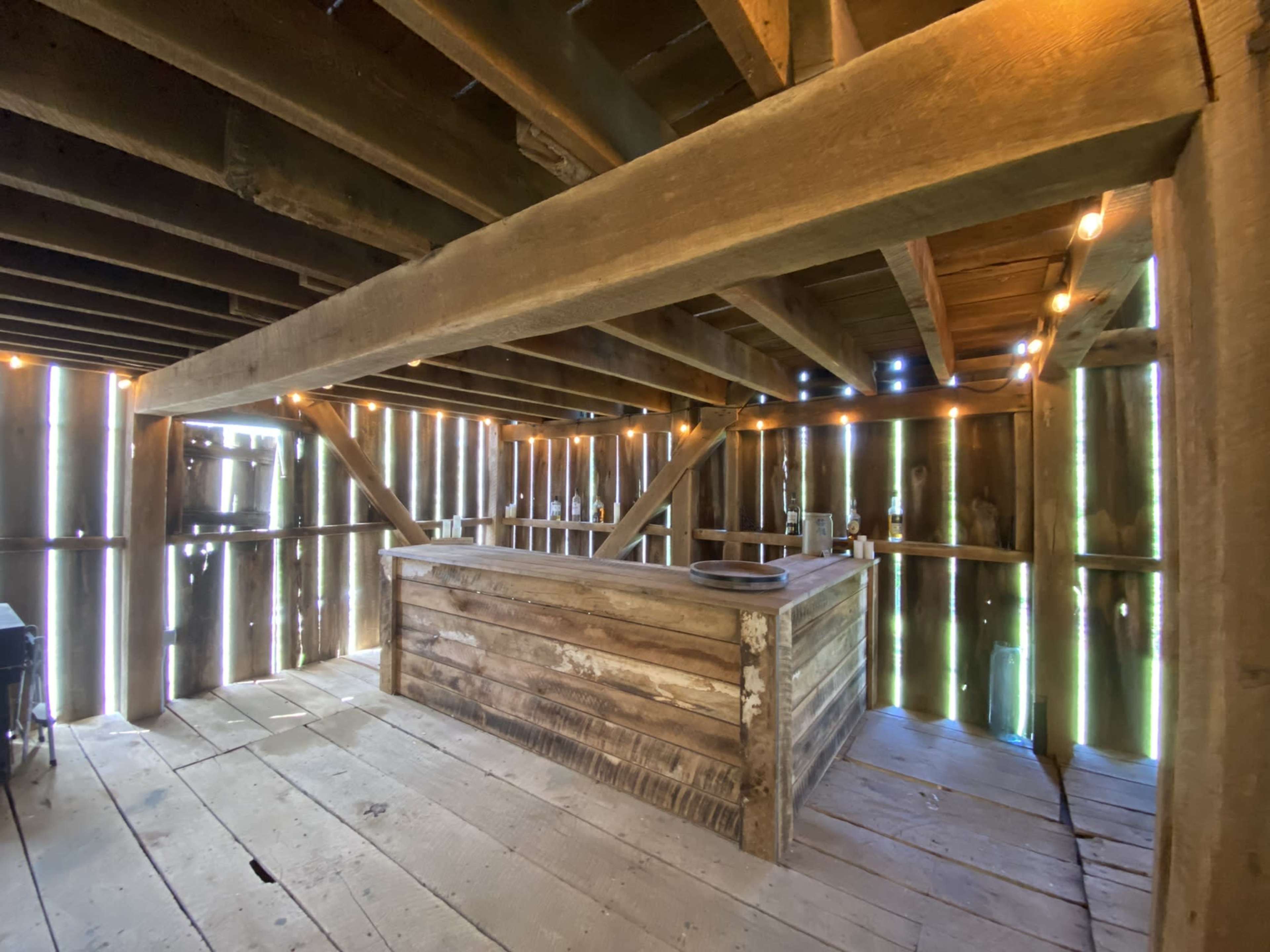 A rustic wooden interior with a bar counter and illuminated walls created by gaps between vertical planks.