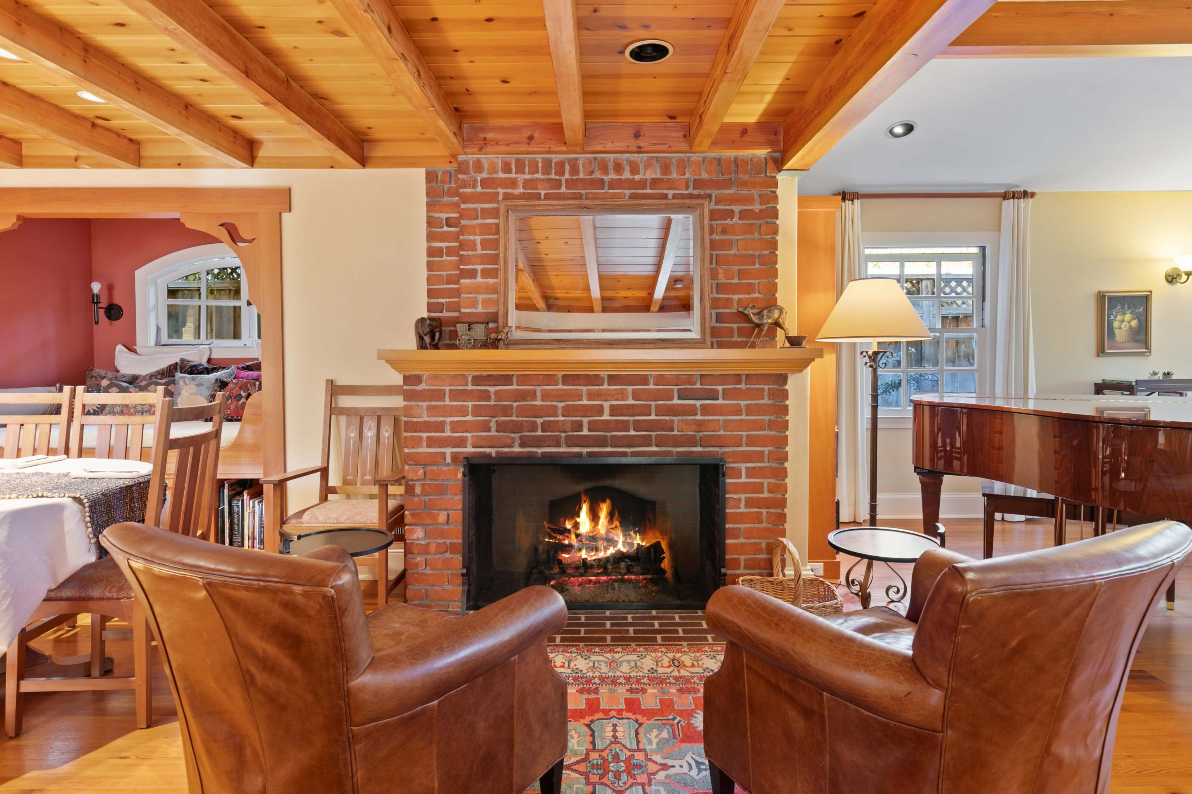 A cozy living room with a brick fireplace, two leather armchairs facing the fire, and wooden beams on the ceiling.