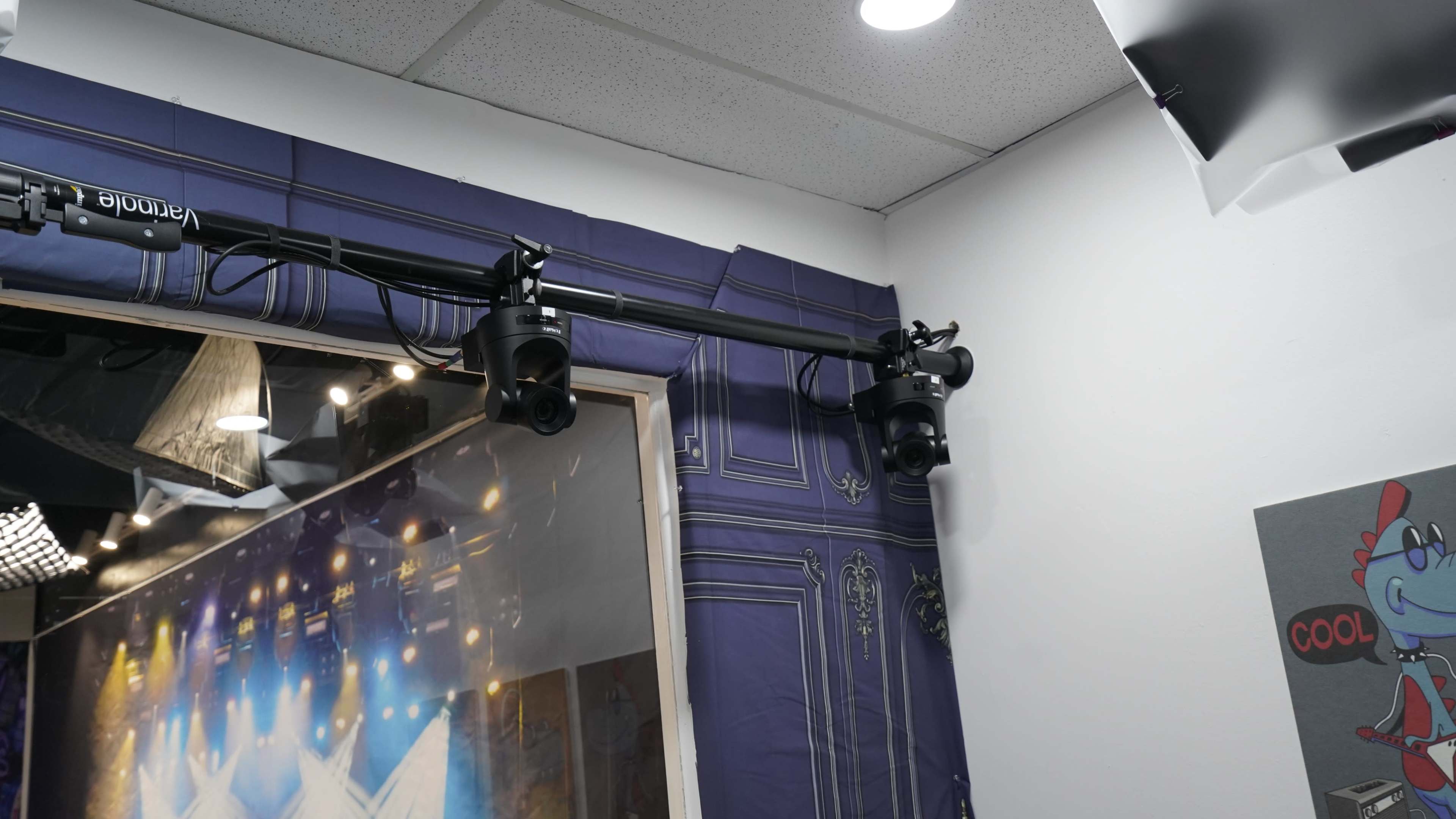 A lighting rig mounted on a ceiling near a wall with textured blue wallpaper, featuring multiple spotlights aimed downwards.