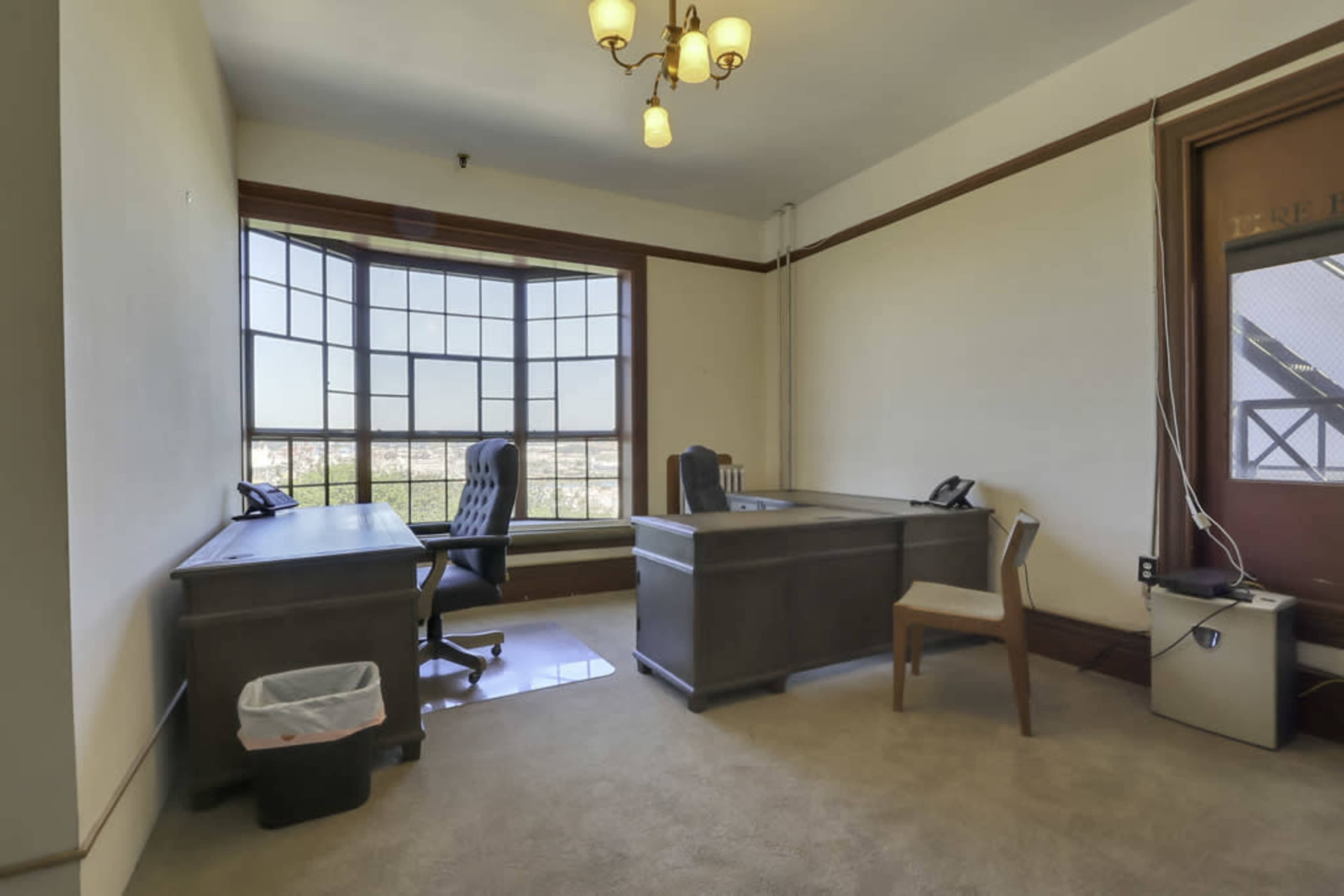 A spacious office with two desks, a chair, and a large window overlooking a view.