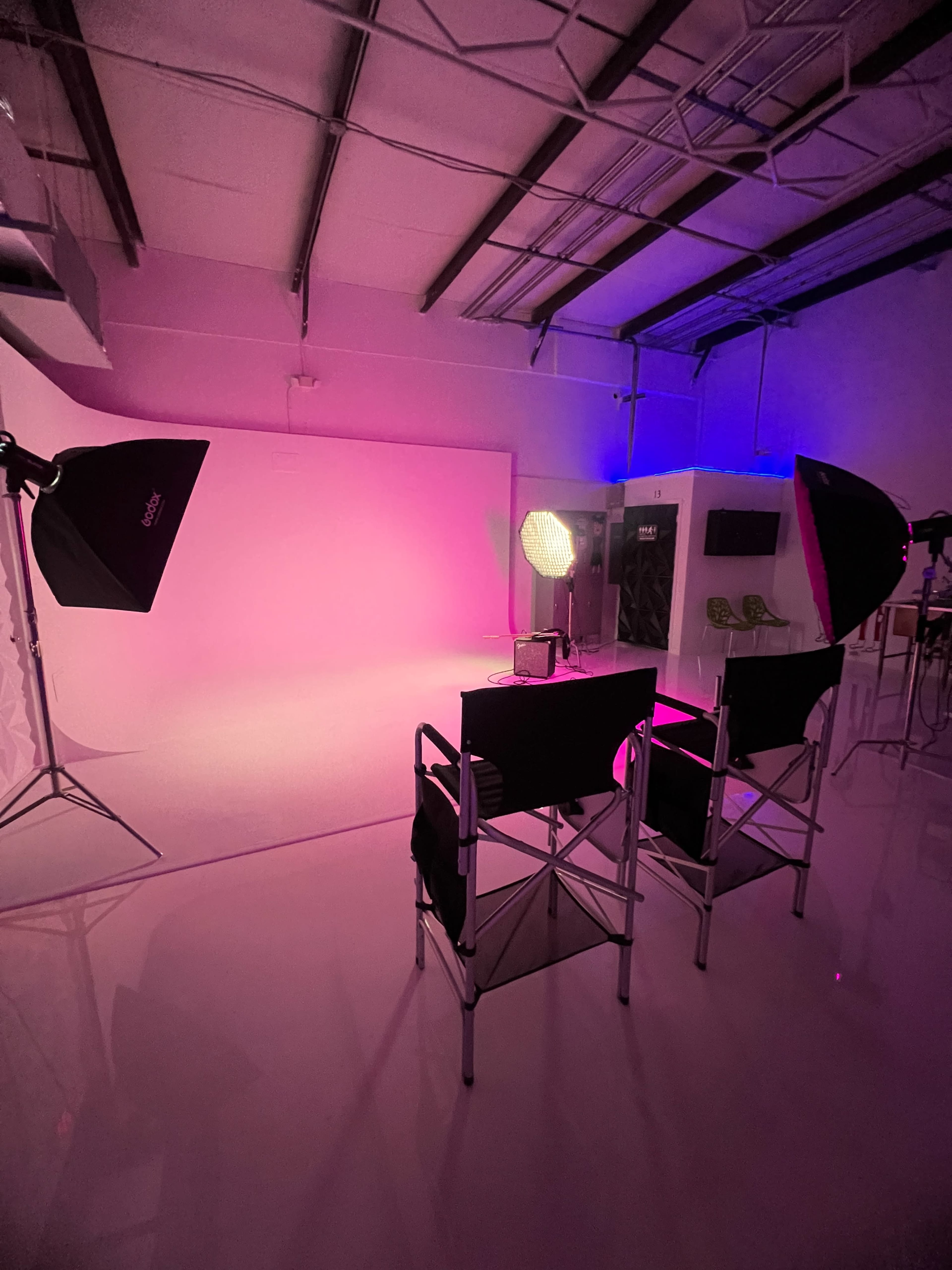 A photography studio with two director's chairs, studio lights, and a blank wall illuminated in pink.