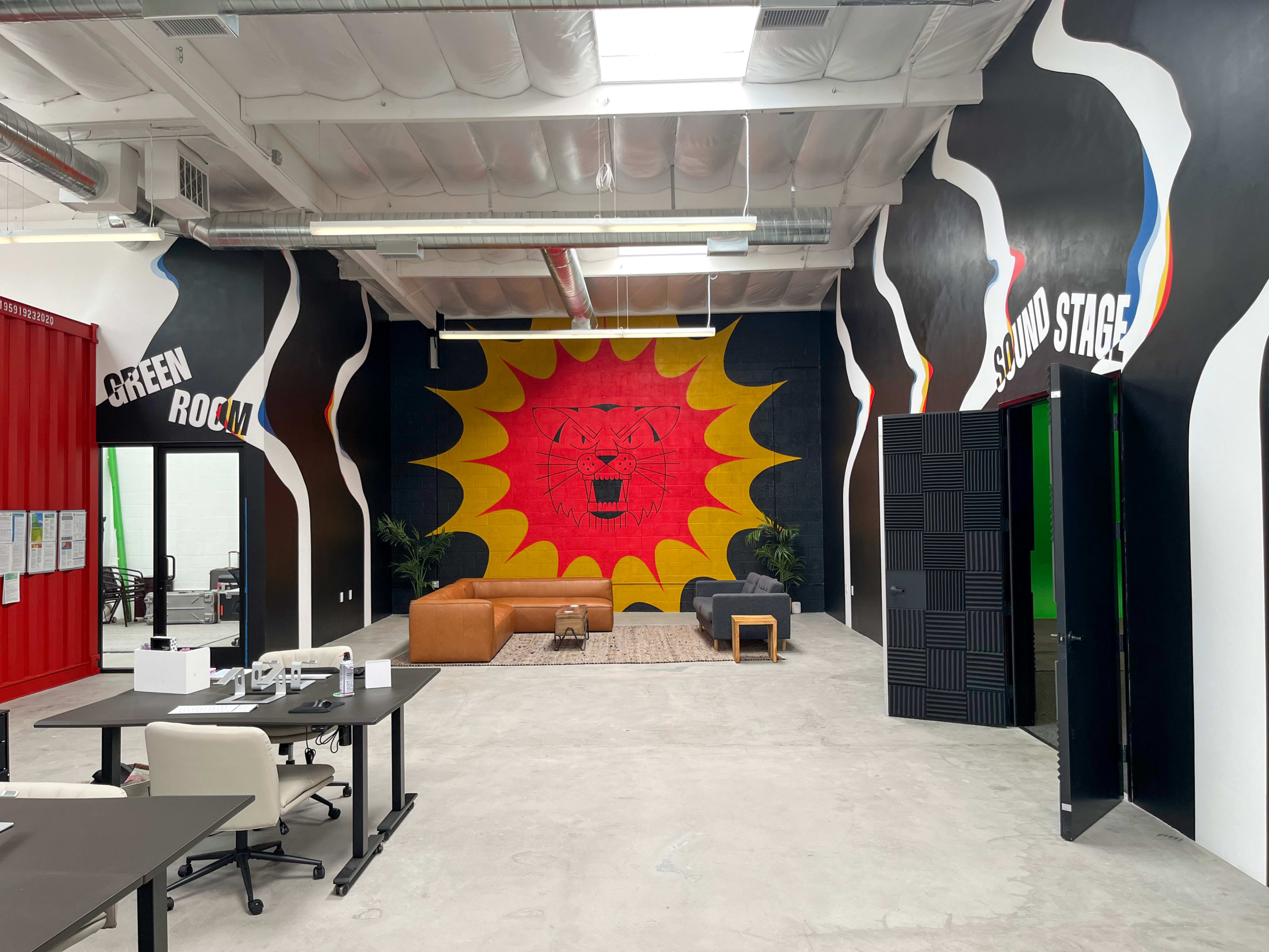 A creative workspace featuring a vibrant mural of a lion's face on the back wall, with designated areas labeled "Green Room" and "Sound Stage" on either side.