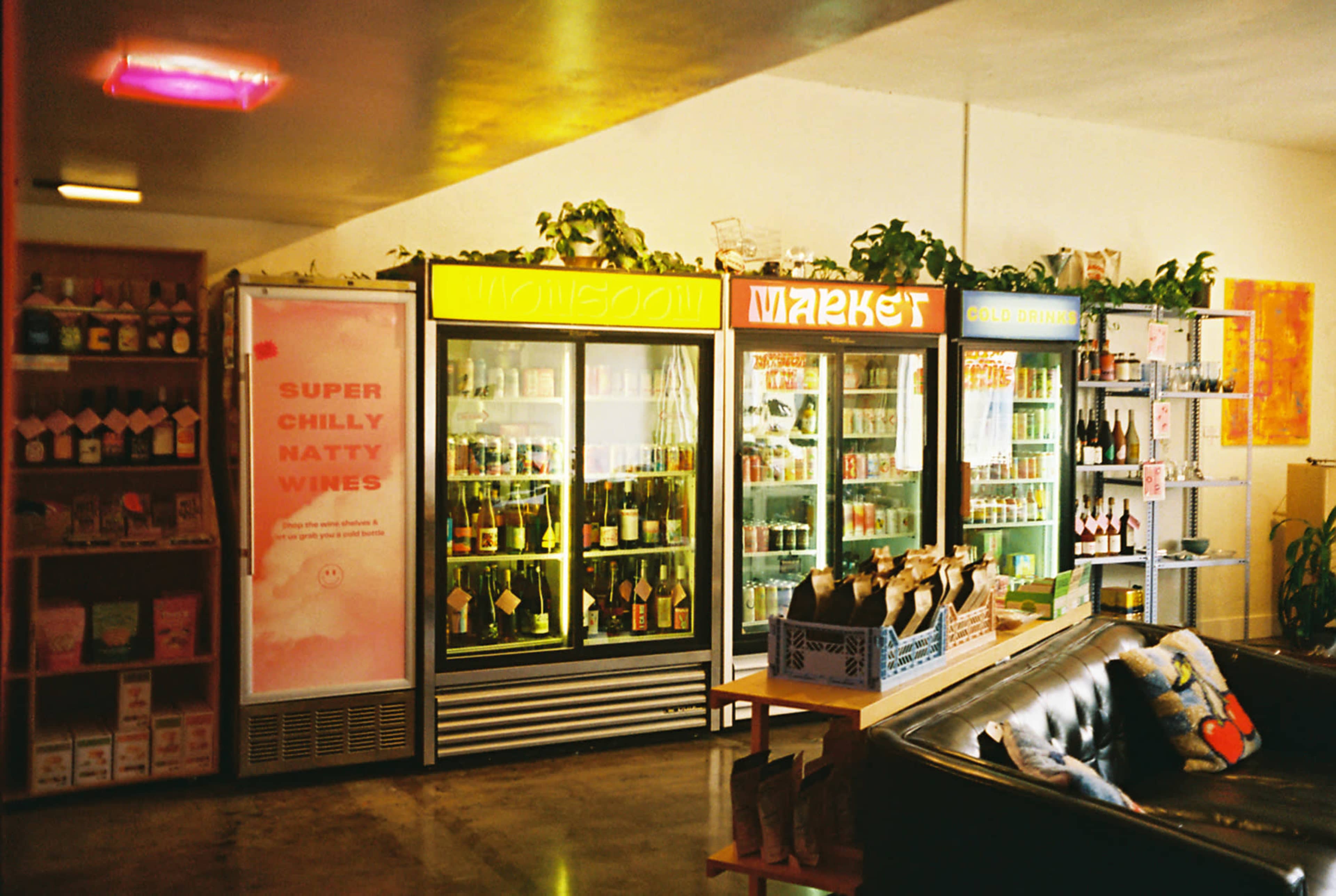 A colorful interior of a store featuring refrigerator units filled with beverages and a display of bottles on a counter.