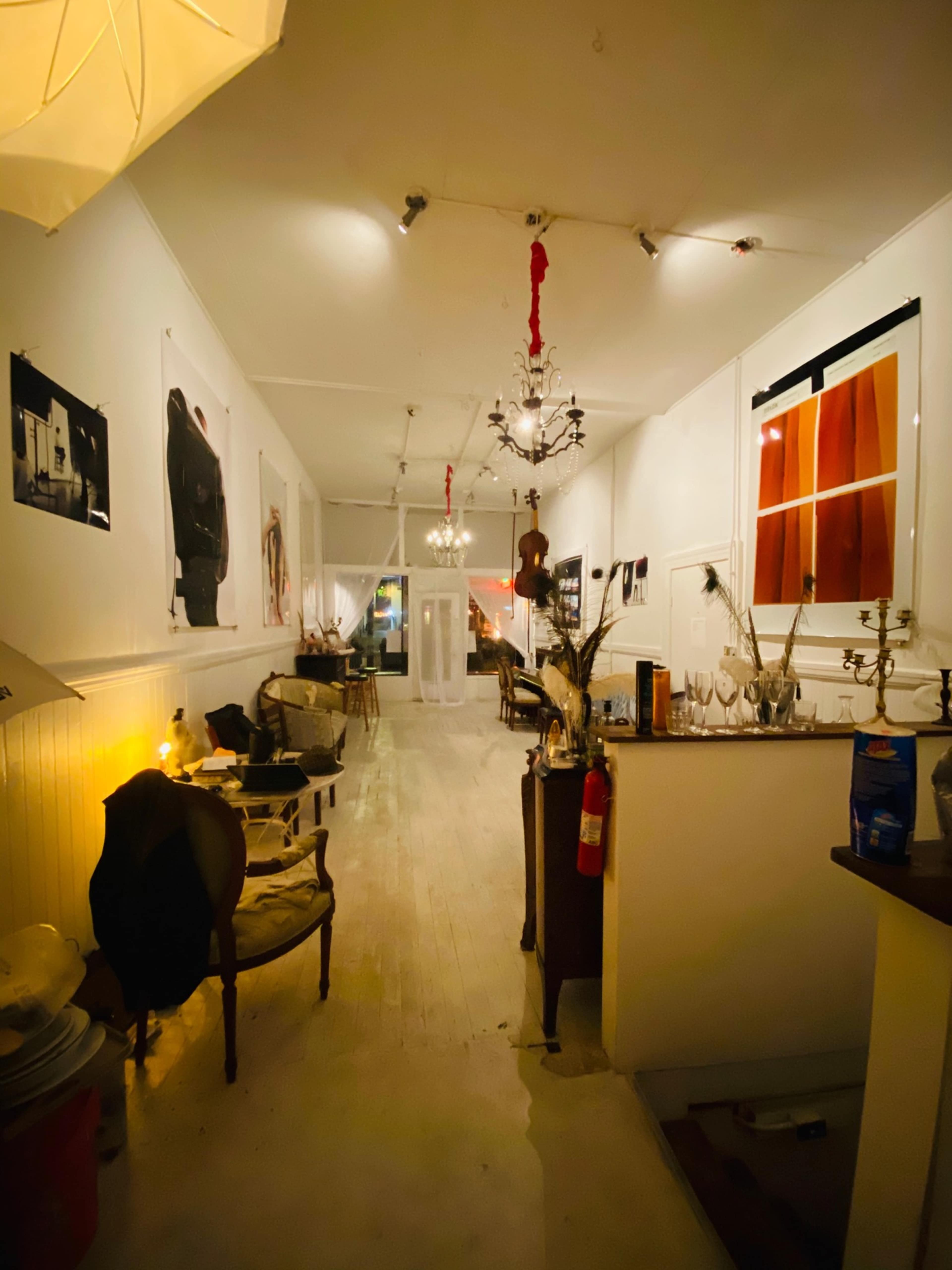 A dimly lit hallway of an art gallery, adorned with various artworks on the walls and illuminated by chandeliers.