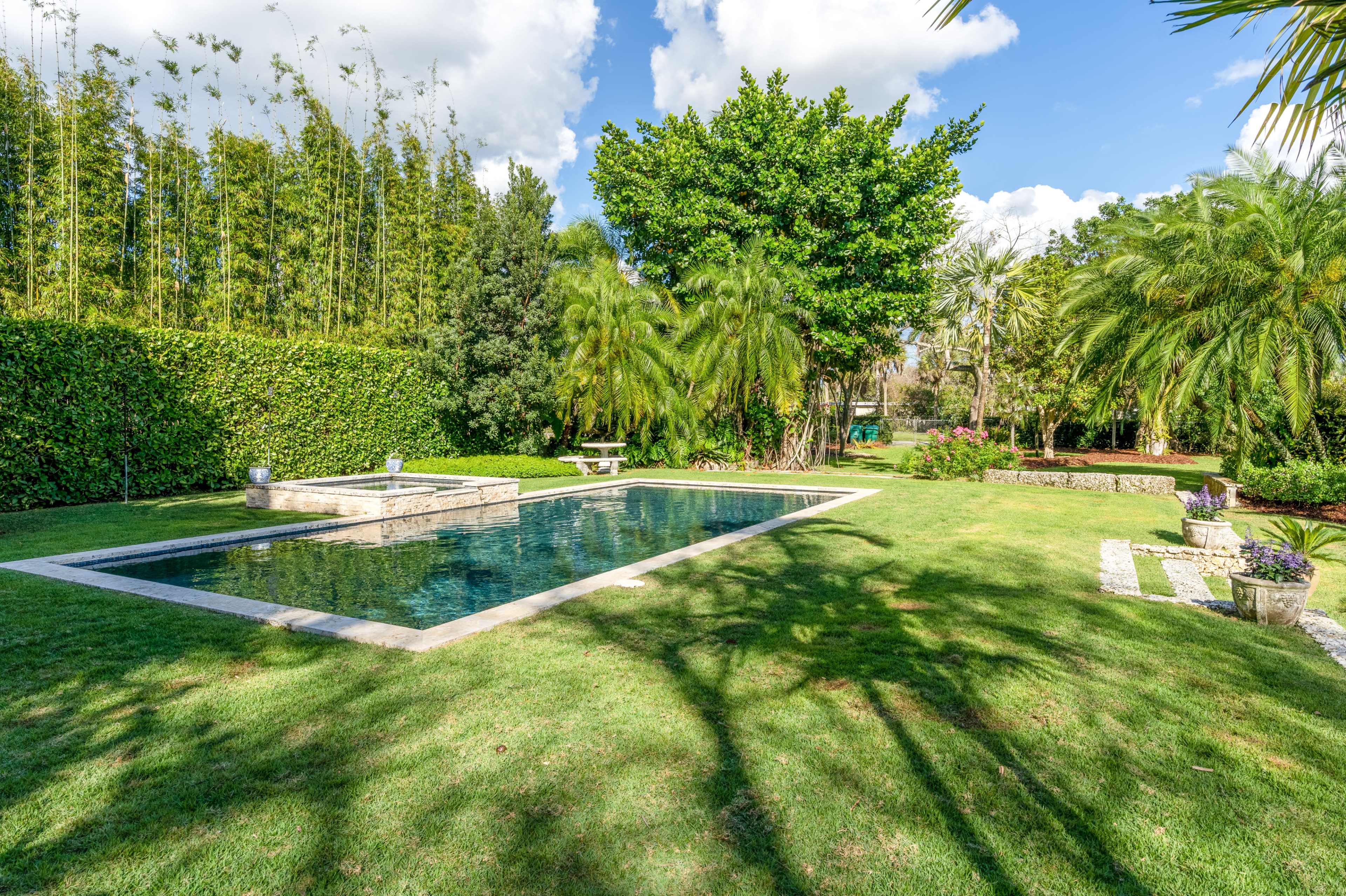 A neatly landscaped backyard features a swimming pool surrounded by lush greenery and various trees.