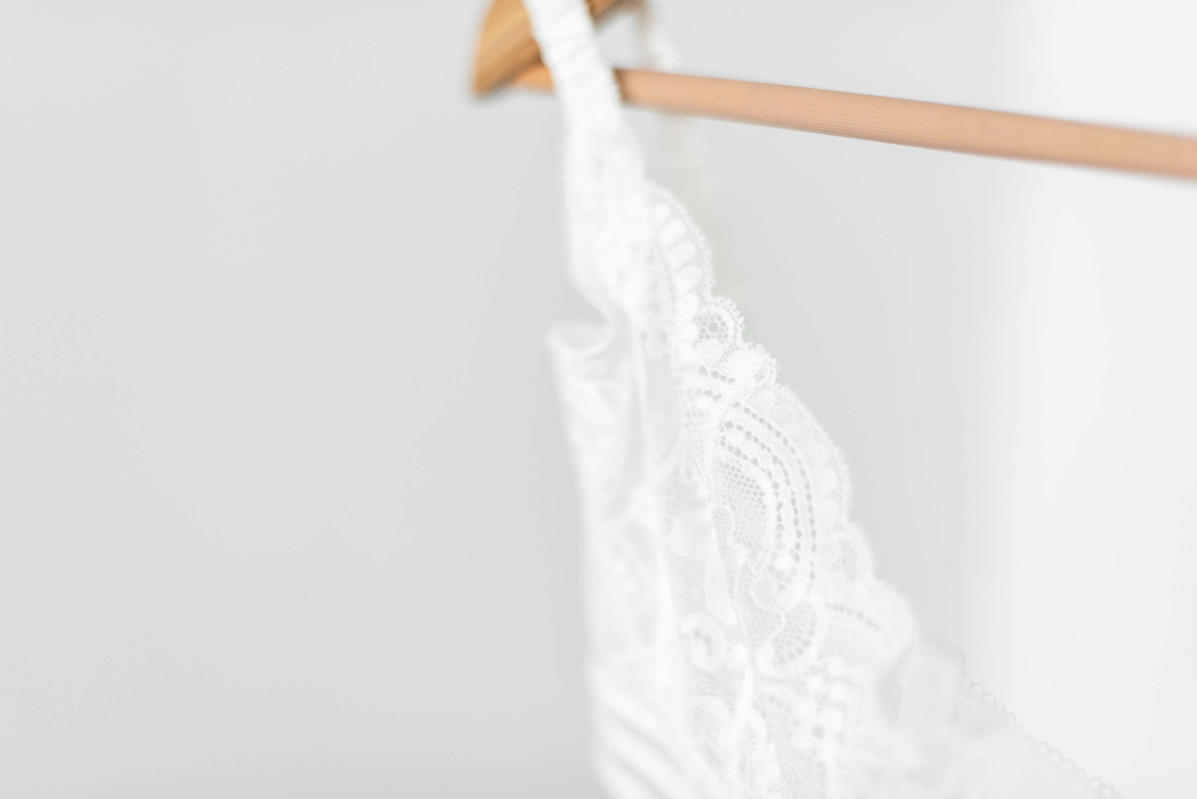 A white lace garment is hung on a wooden hanger against a light gray background.