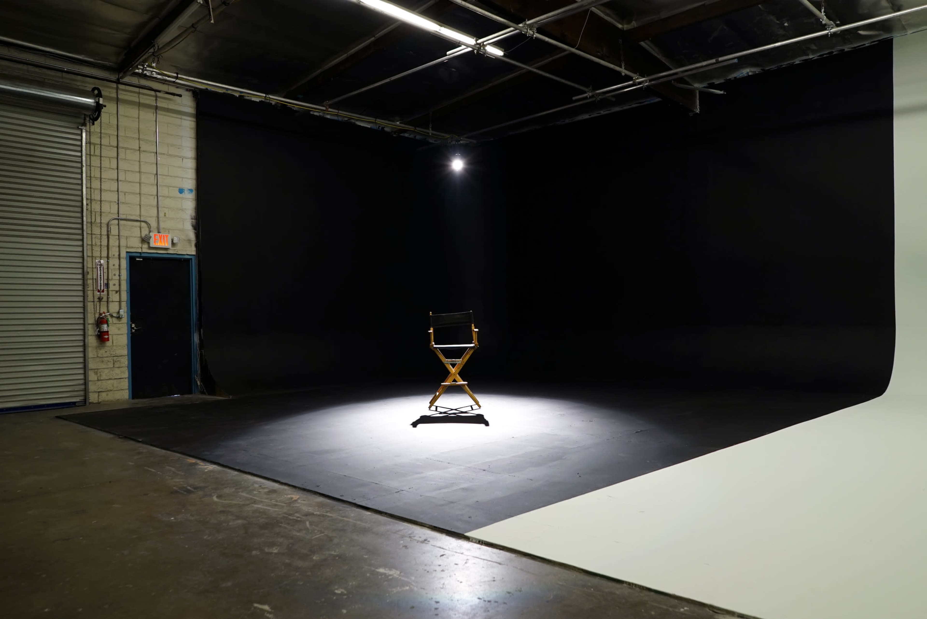 A single director's chair is illuminated in a dark studio space with a gray backdrop.