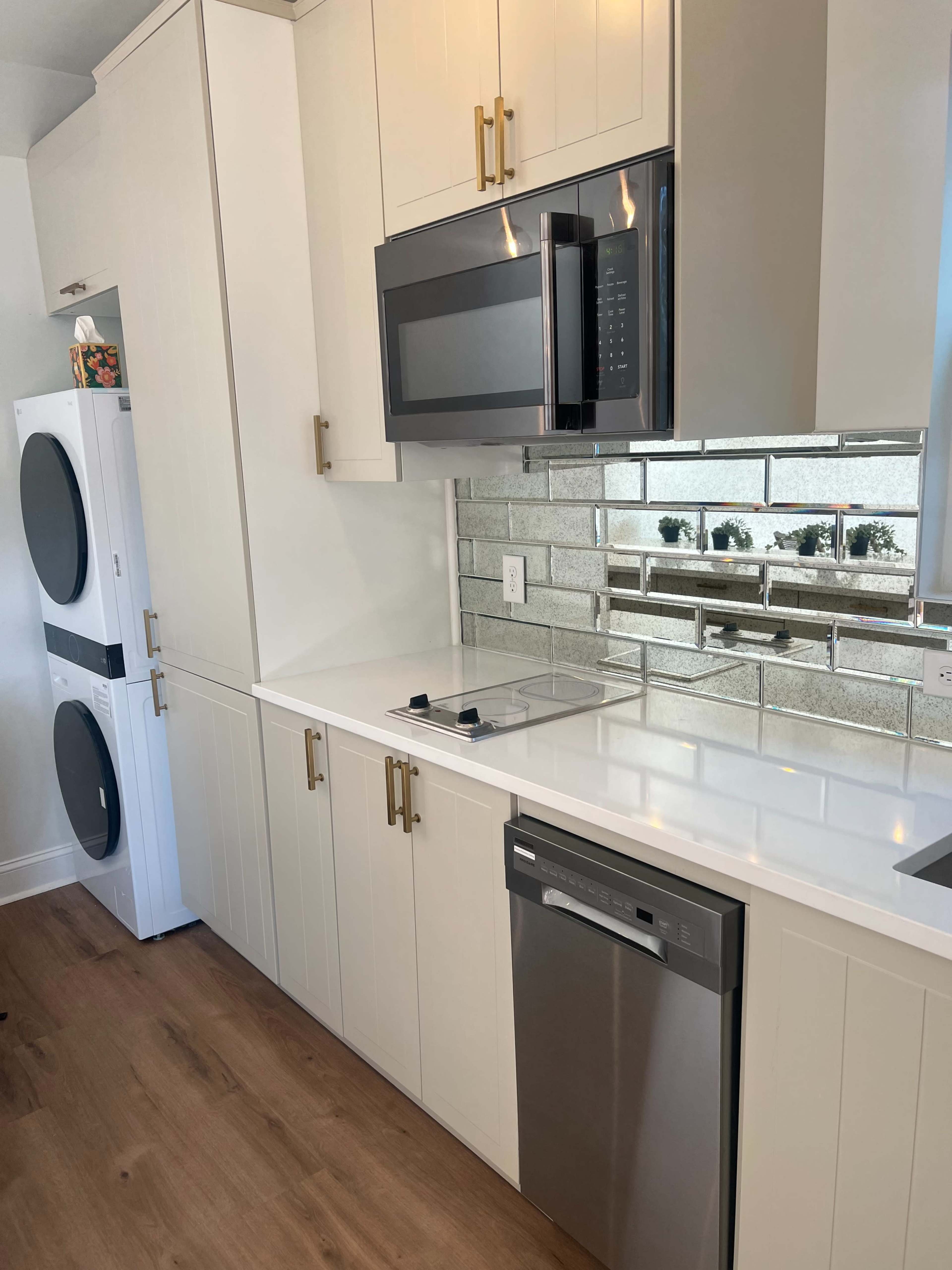 The image shows a modern kitchen featuring white cabinetry, a built-in microwave above a stovetop, a stainless steel dishwasher, and a washer and dryer combination adjacent to the cabinetry.