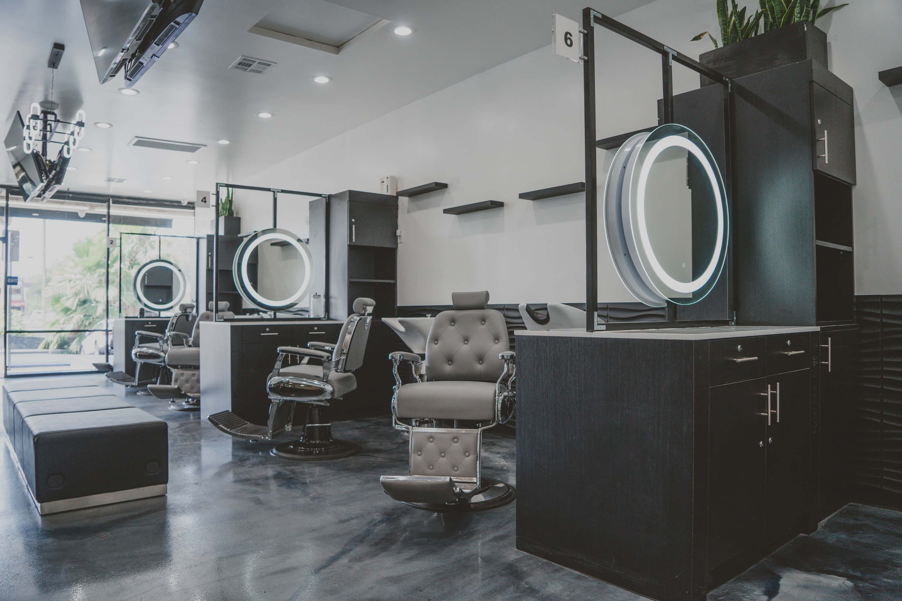 A modern barbershop interior with several styling stations featuring mirrors and illuminated circular lights, along with barber chairs arranged neatly.