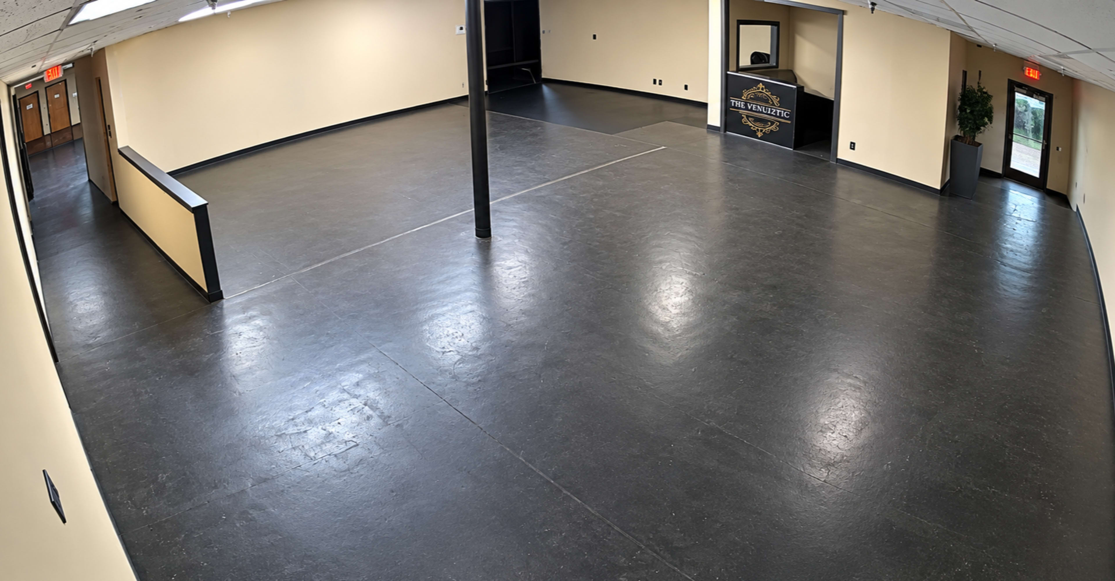 The image shows a spacious, empty interior room with a polished black floor, a reception area in the rear, and doors leading outside.