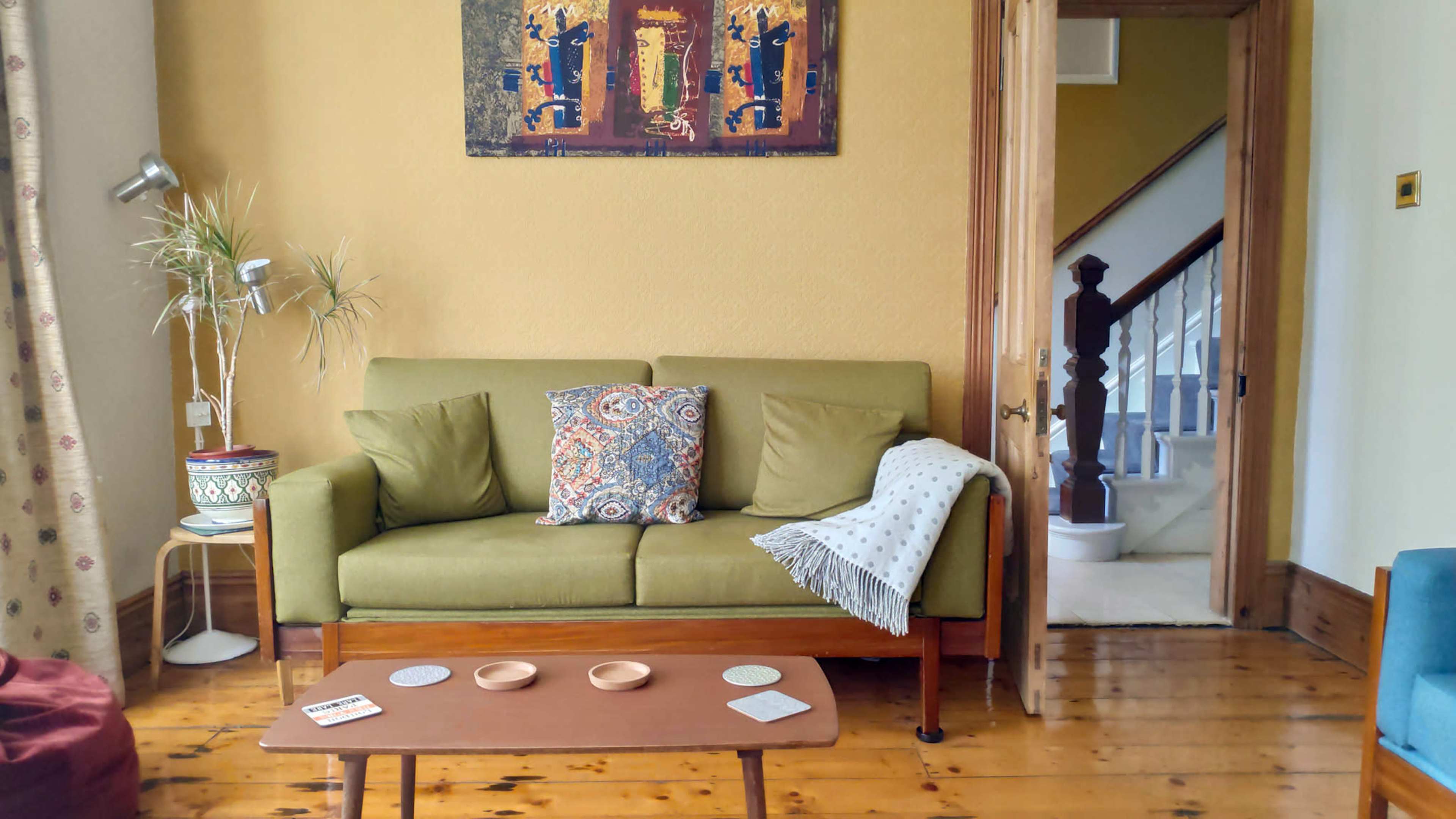 A cozy living room with a green sofa, decorative pillows, a wooden coffee table, and a doorway leading to a staircase.