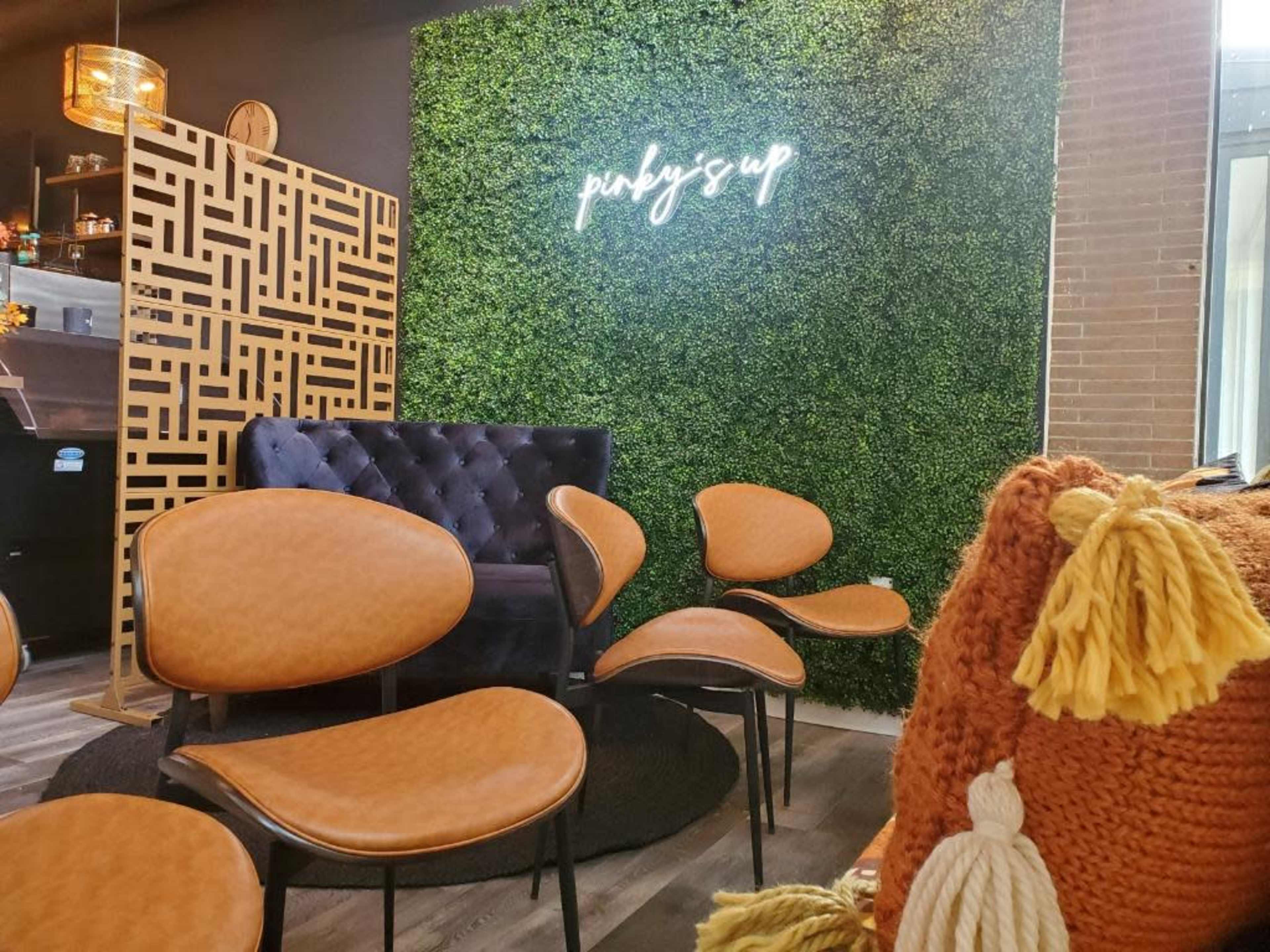 A cozy interior space with a greenery wall featuring a neon sign, modern upholstered chairs, and a textured orange throw.