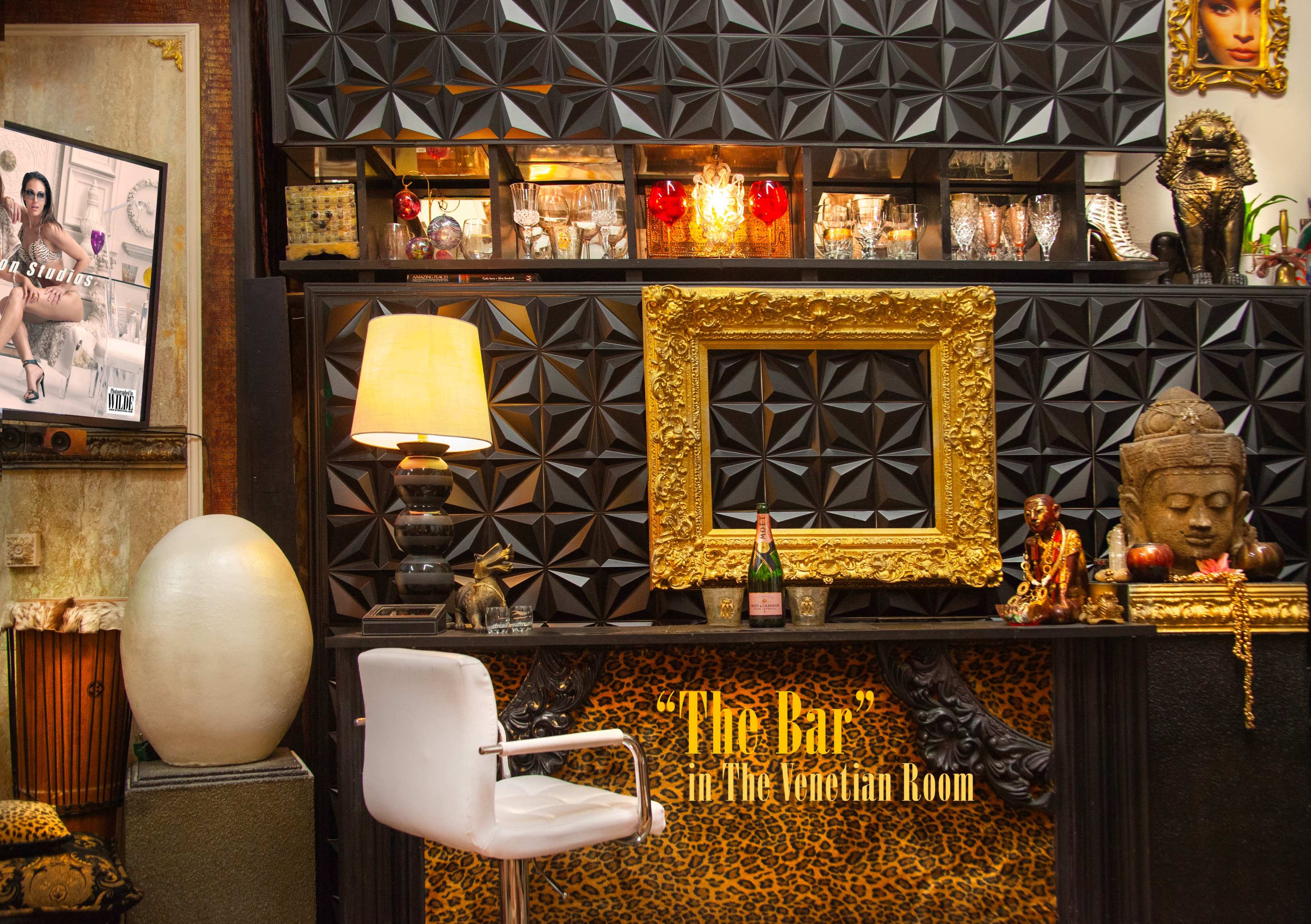 The image shows a stylish bar area adorned with decorative elements, including a large ornate frame, a statue, and various glassware displayed on shelves.
