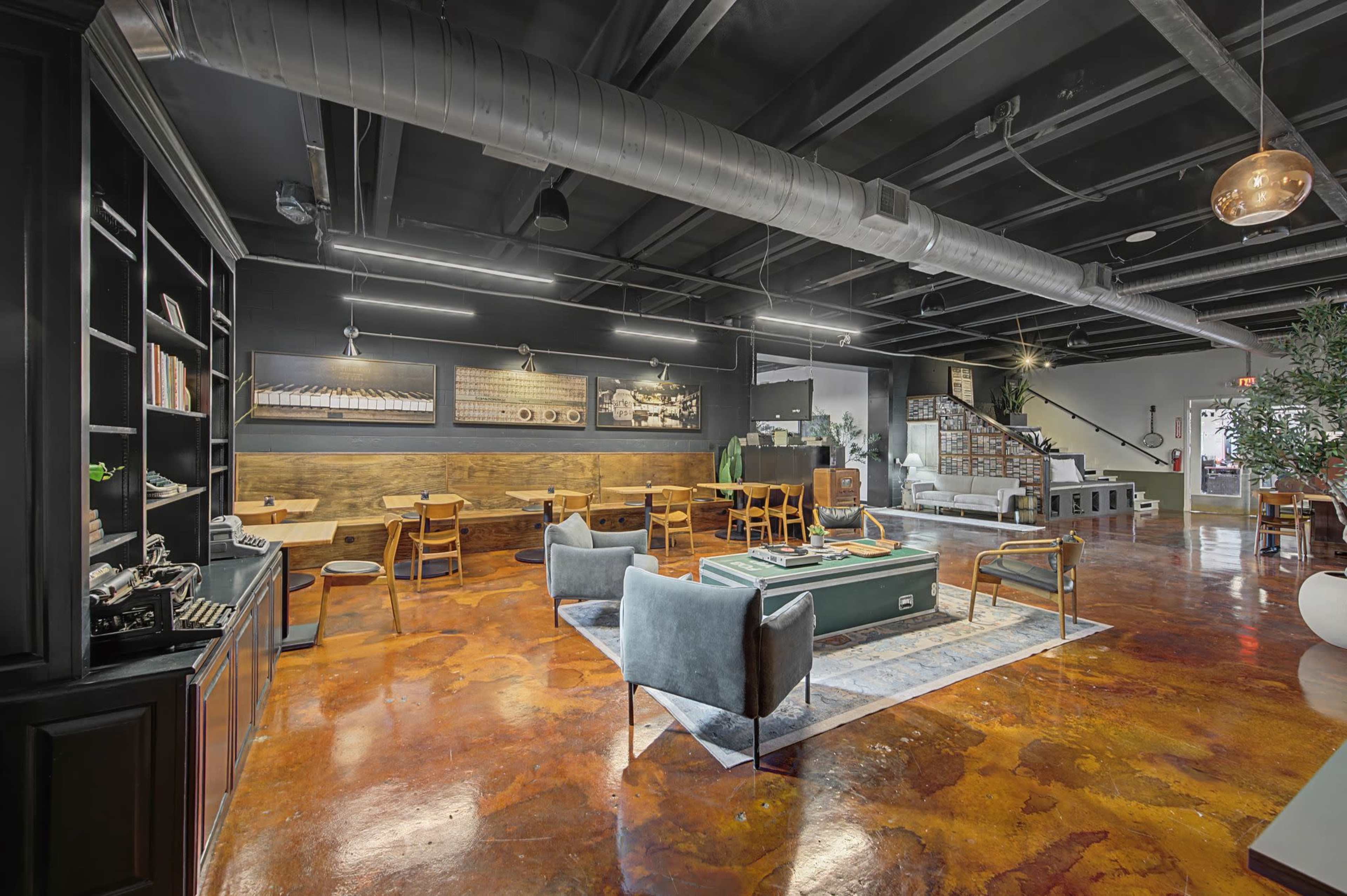 The image shows a spacious modern lounge area featuring wooden tables, comfortable seating, a pool table, and industrial-style decor.
