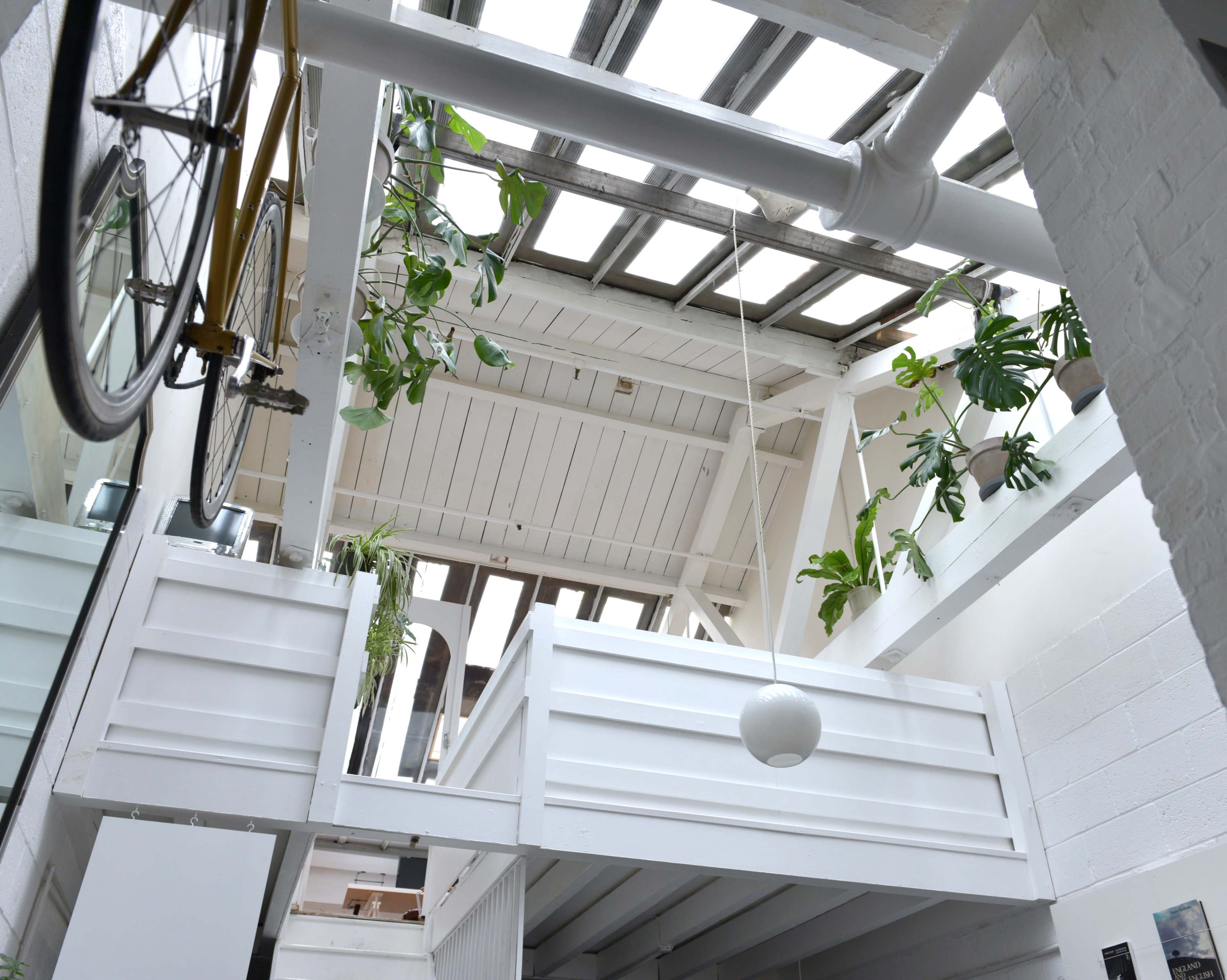 A bright, airy interior space with a loft area, large windows, and hanging plants.