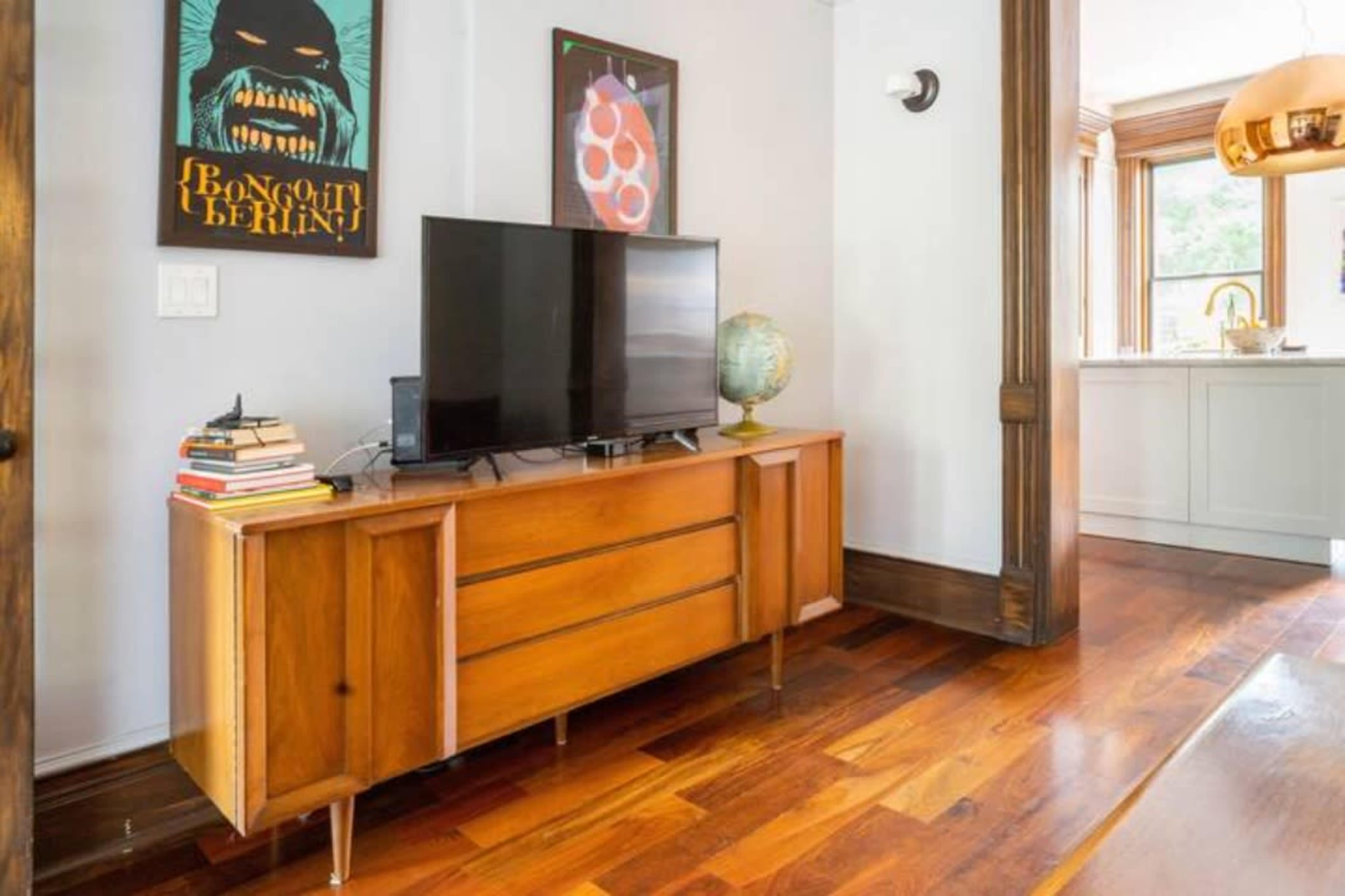 The image shows a modern living room with a wooden television stand, a globe, books, and framed artwork on the walls.