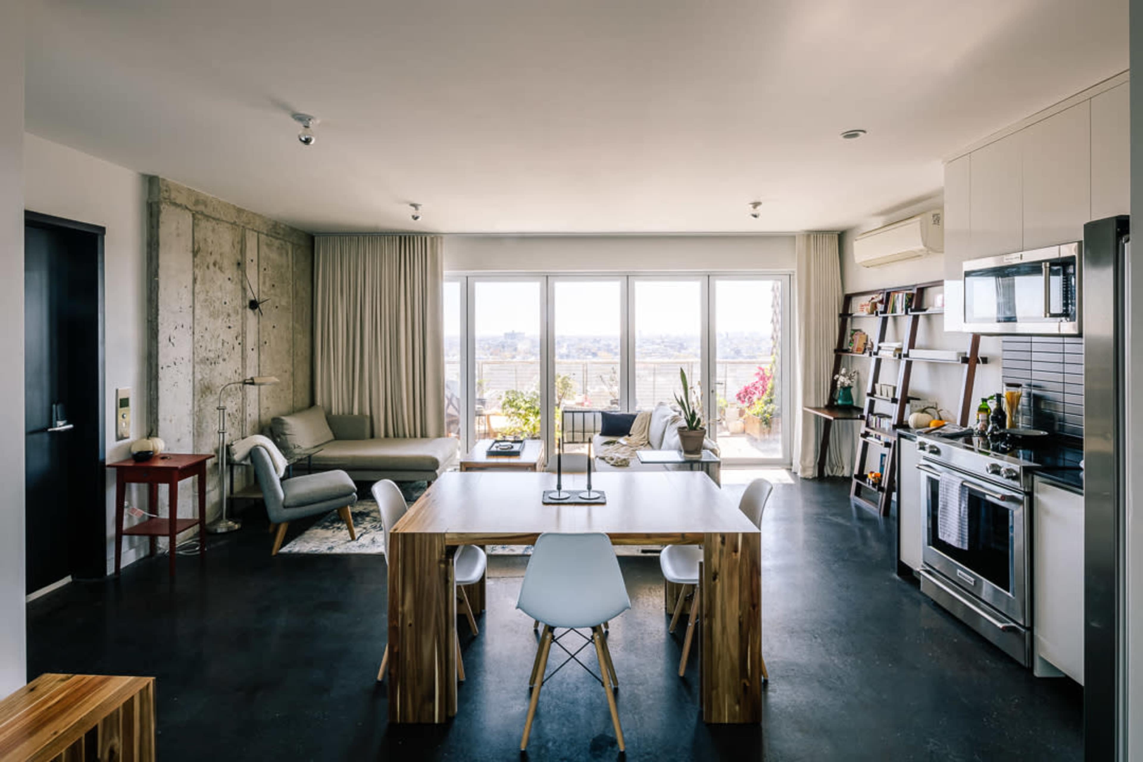 The image shows a modern open-concept kitchen and living area with a dining table, chairs, and large windows overlooking a view.