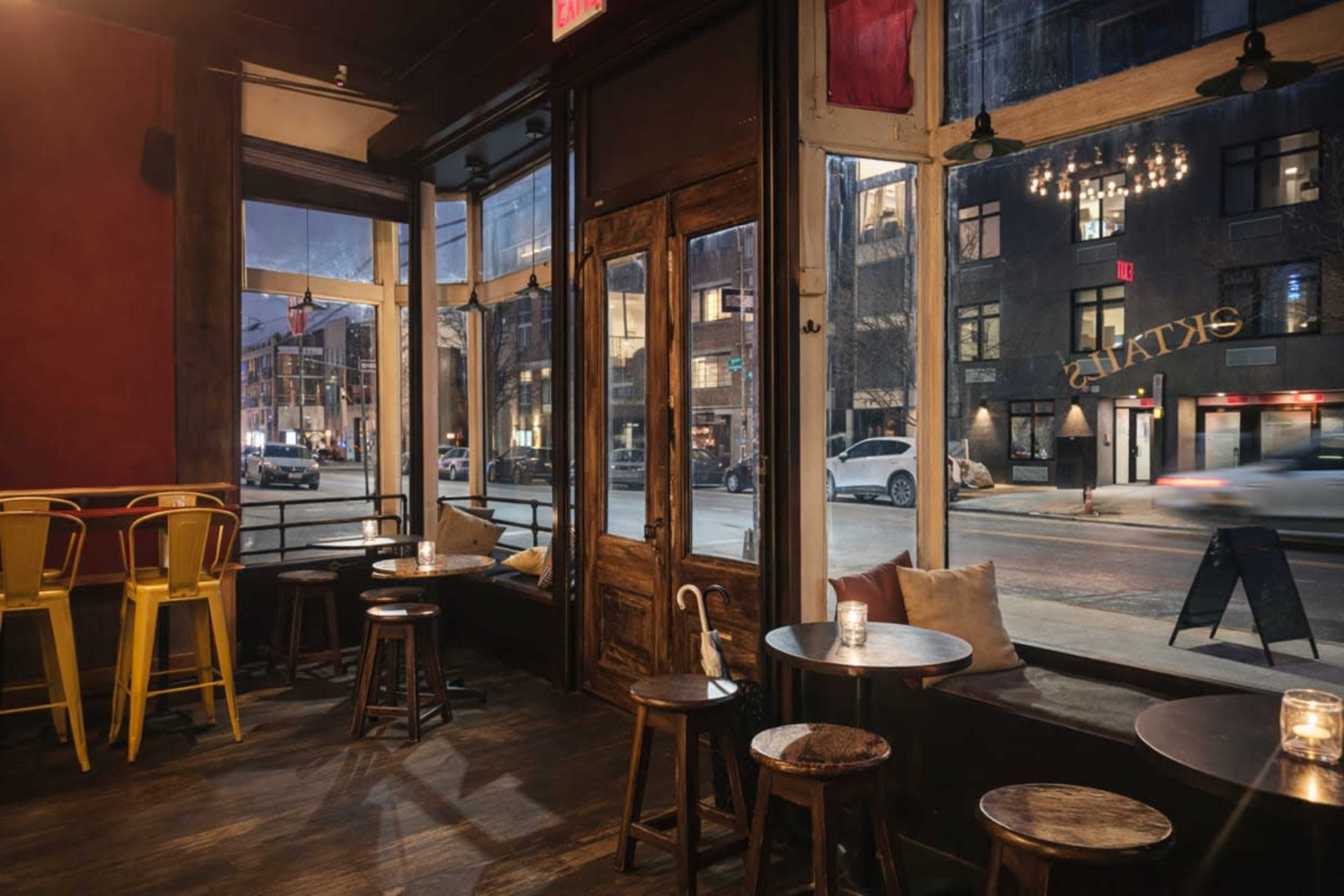 The interior of a dimly lit café features wooden furniture, large windows with street views, and a warm ambiance created by candlelight.